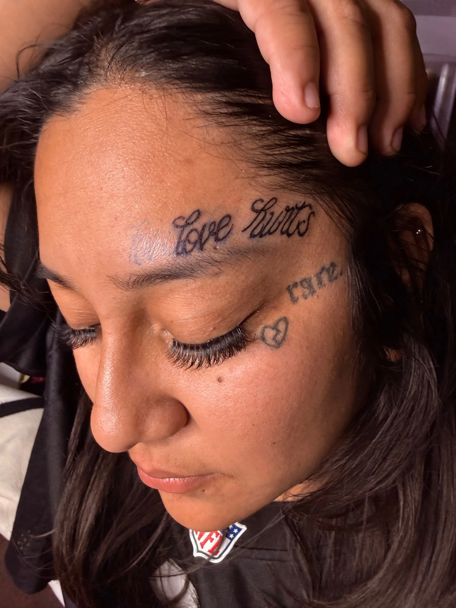 Black script lettering tattoo on forehead with cursive text design