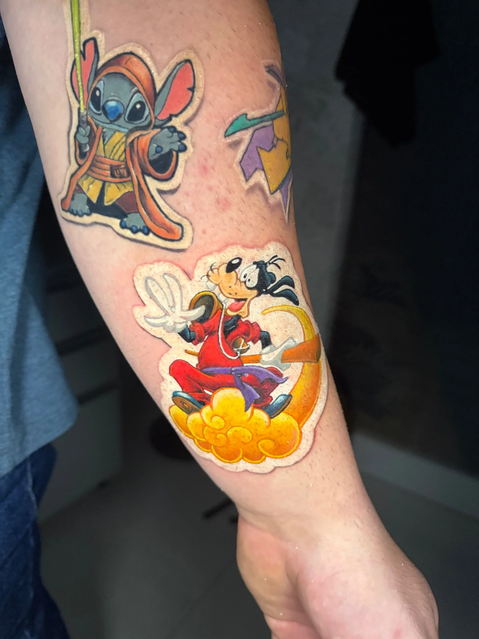 Colorful Disney character sticker-style patchwork tattoo on forearm