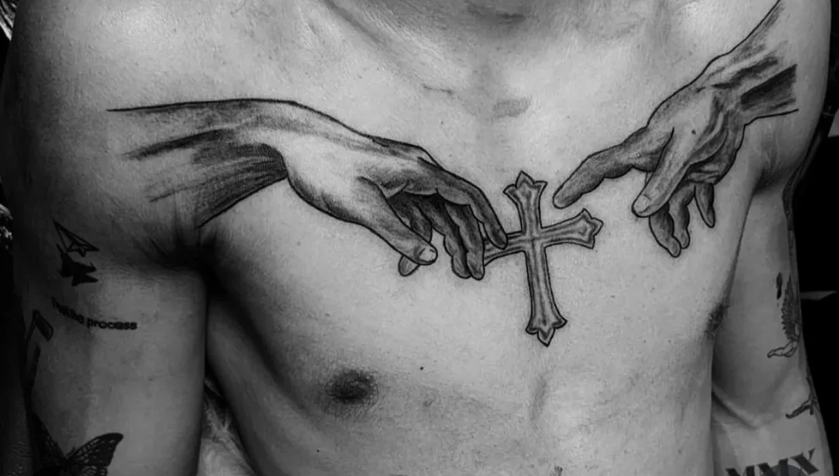 Black and grey realism chest tattoo of two hands holding a cross