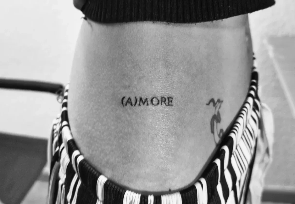 Bold serif lettering tattoo on stomach with astrological symbol