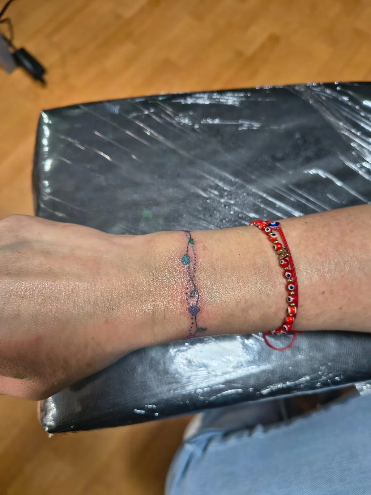 Fine line bracelet tattoo with floral accents on wrist