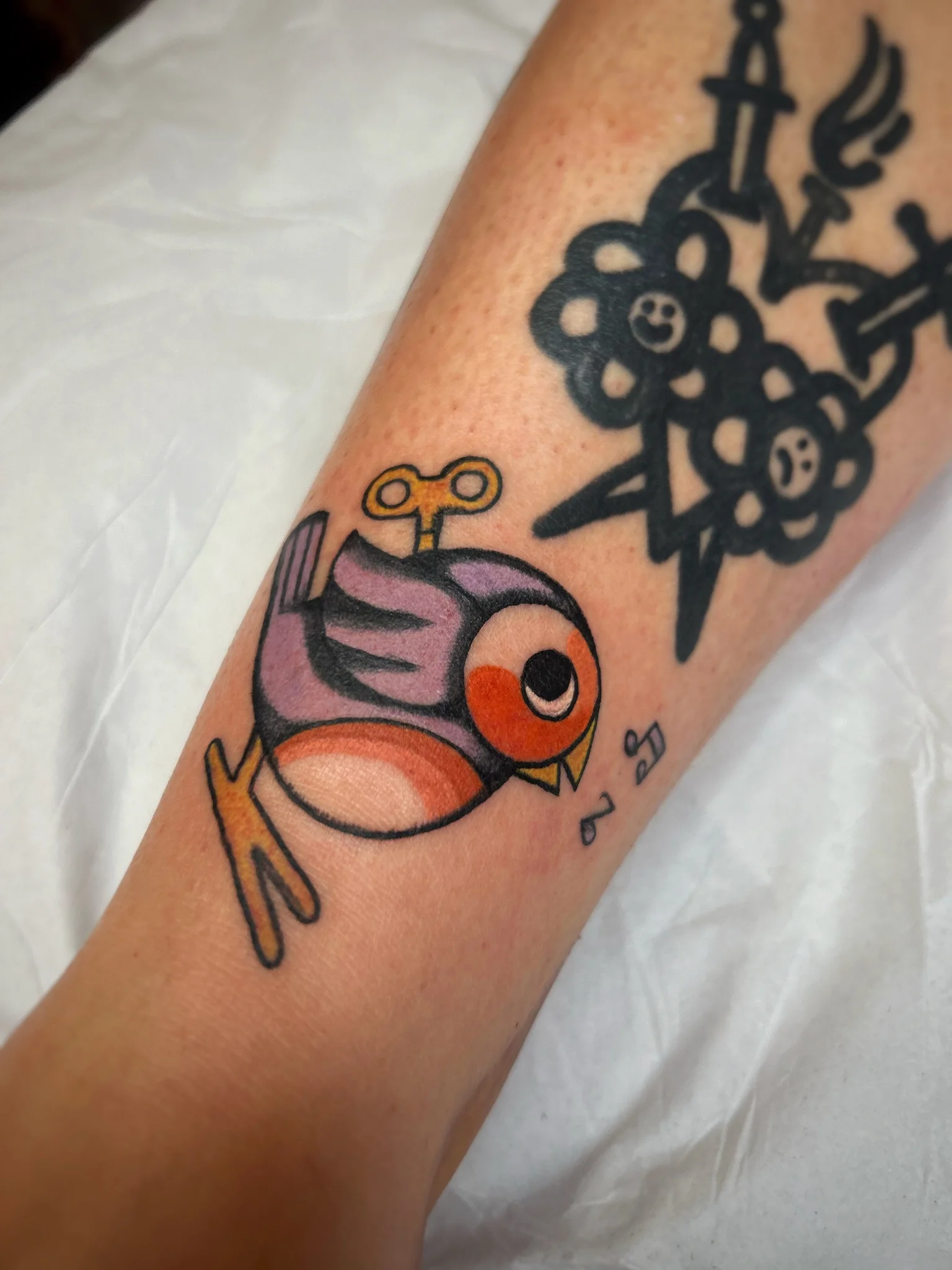 Colorful wind-up toy bird tattoo on forearm