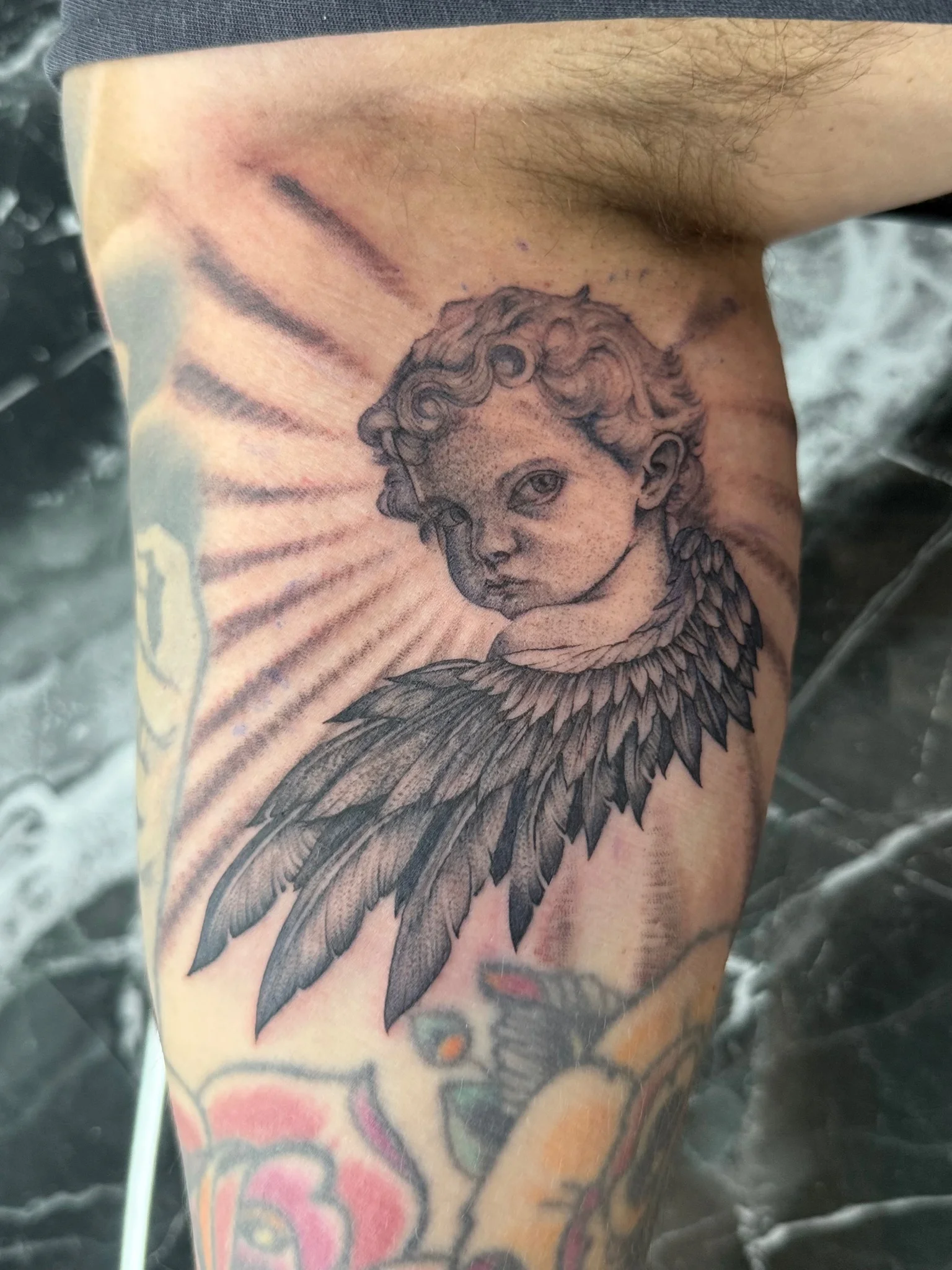 Black and grey cherub with wings tattoo on upper arm