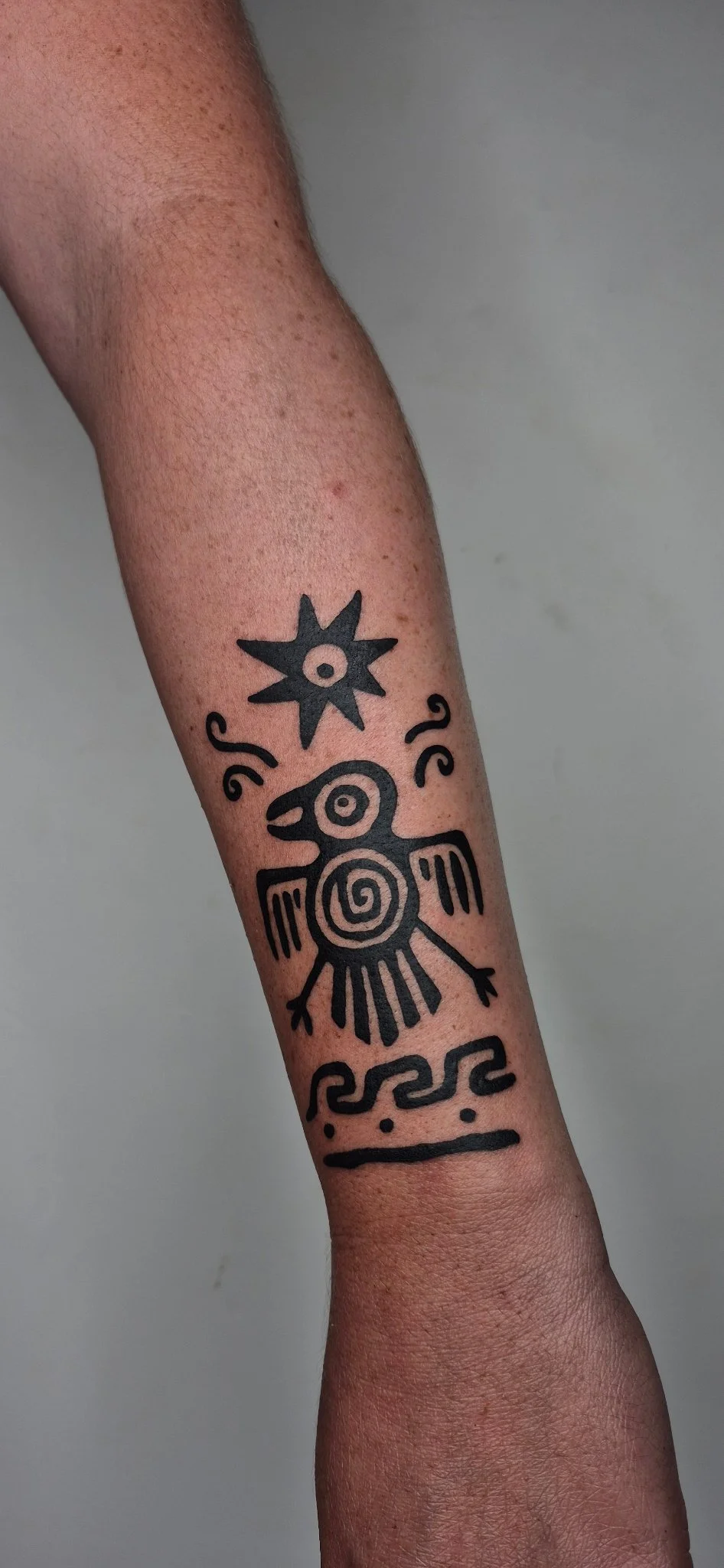 Mesoamerican-style bird and sun symbol tattoo on forearm