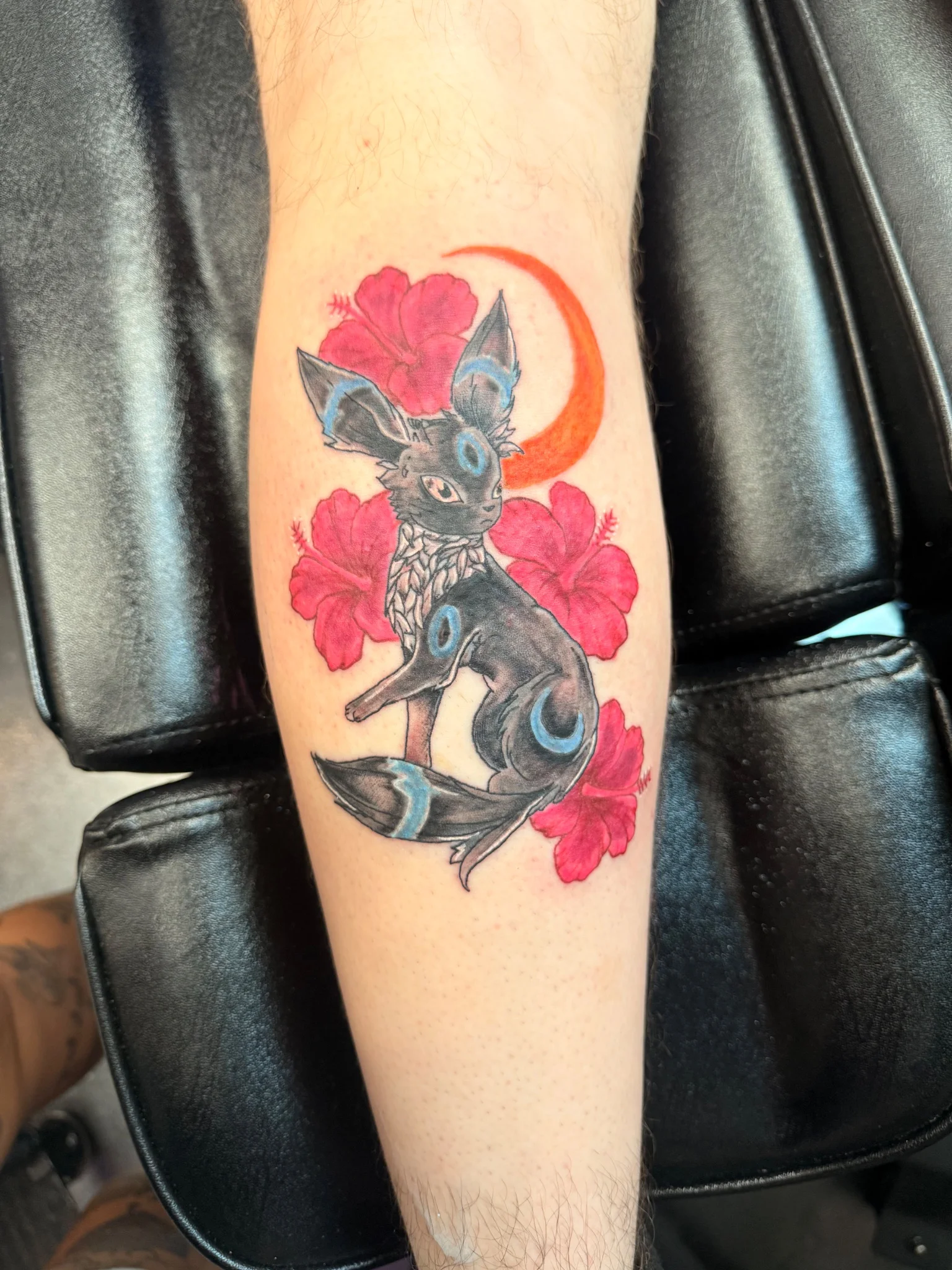 Neo-traditional Umbreon tattoo with hibiscus flowers on lower leg