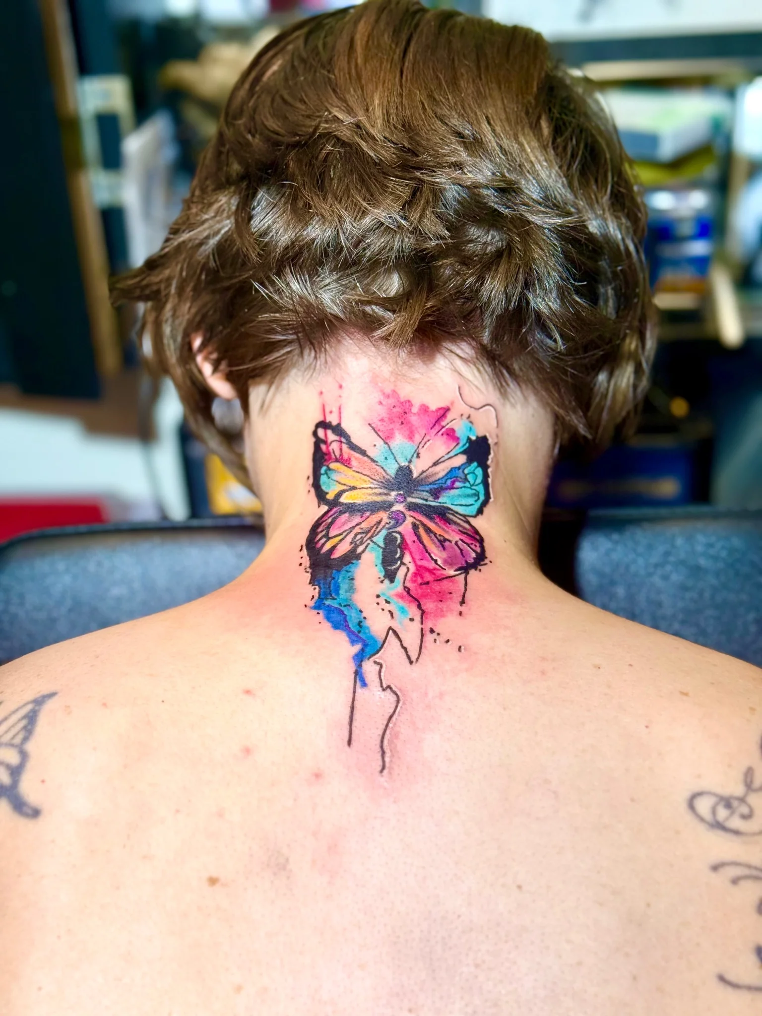 Vibrant watercolor butterfly tattoo on the back of neck