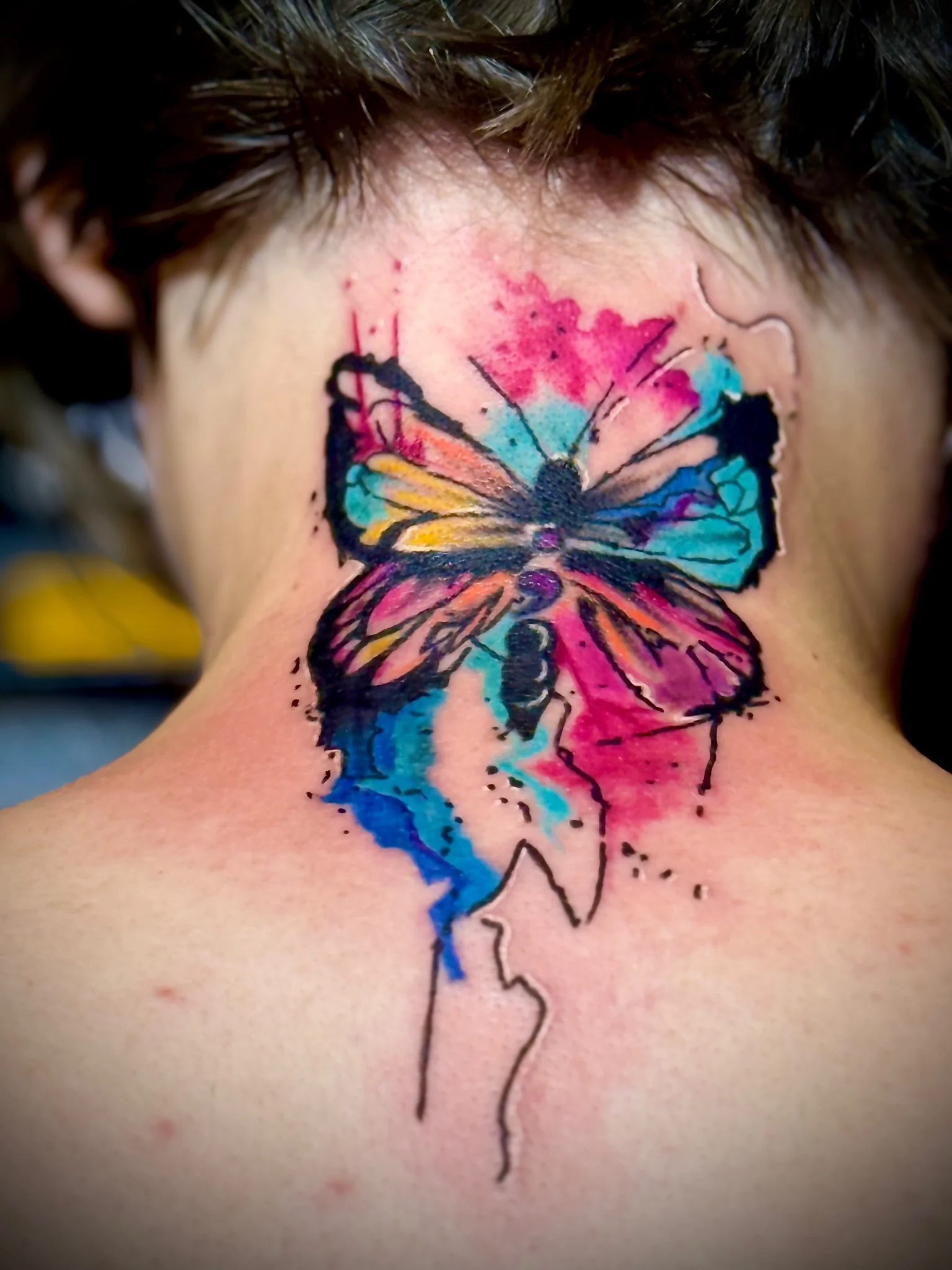Colorful watercolor butterfly tattoo on the back of neck