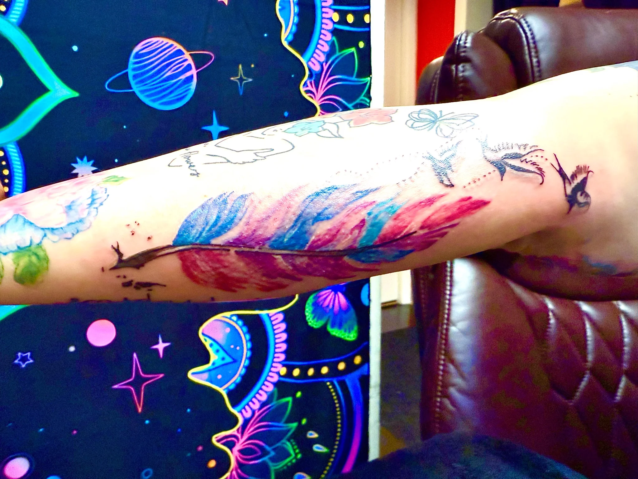 Colorful watercolor feather and swallow tattoo on forearm