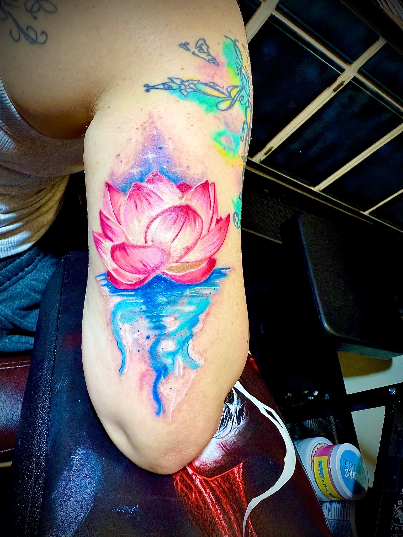 Watercolor lotus flower tattoo with reflection on upper arm