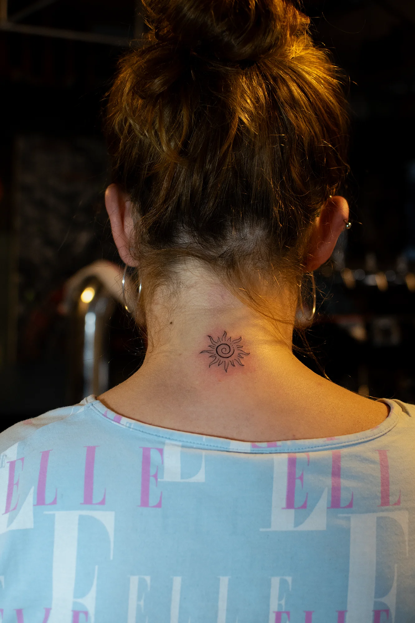 Fine line sun with spiral center tattoo on back of neck