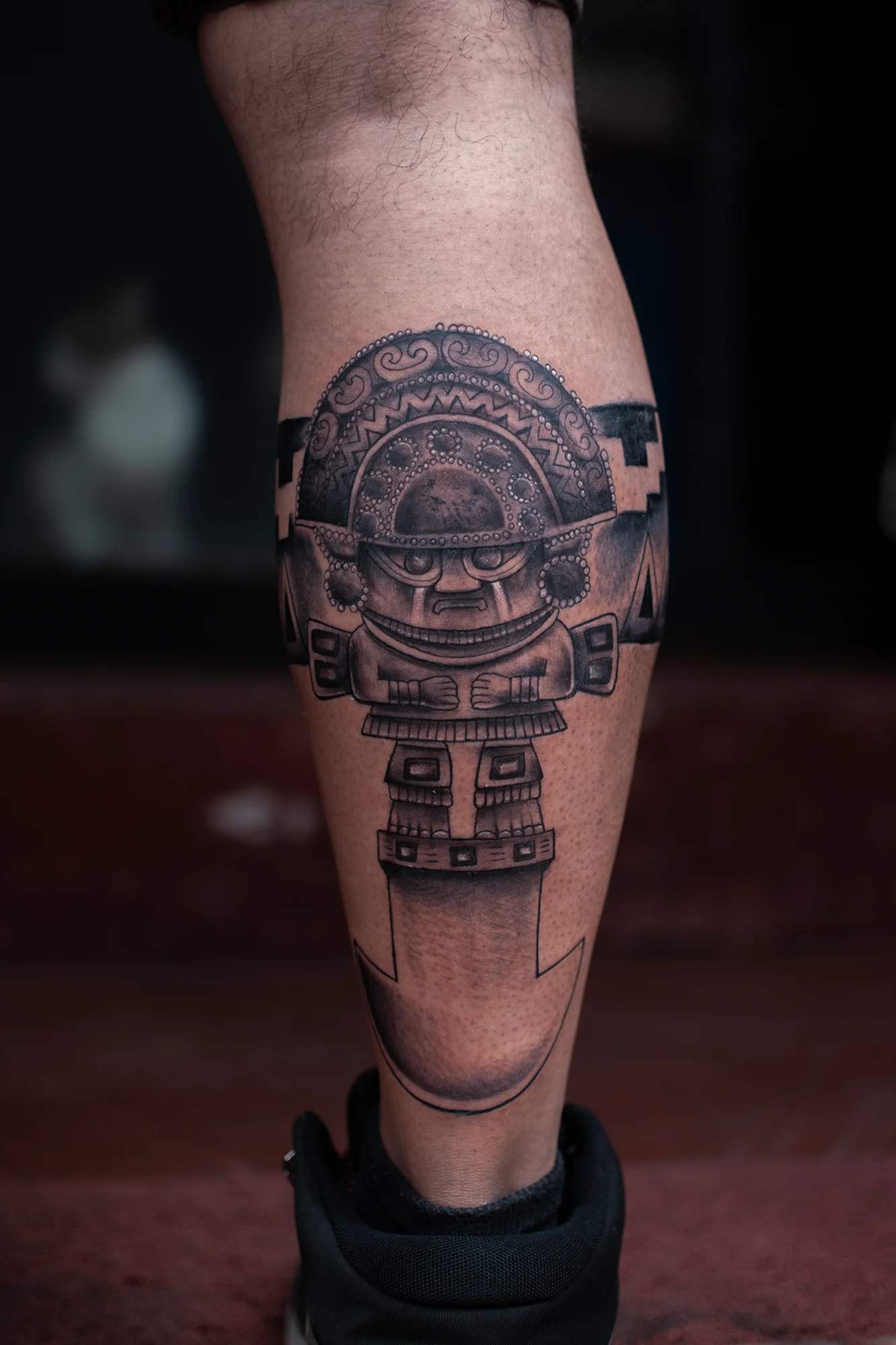 Black and grey pre-Columbian deity figure tattoo on calf