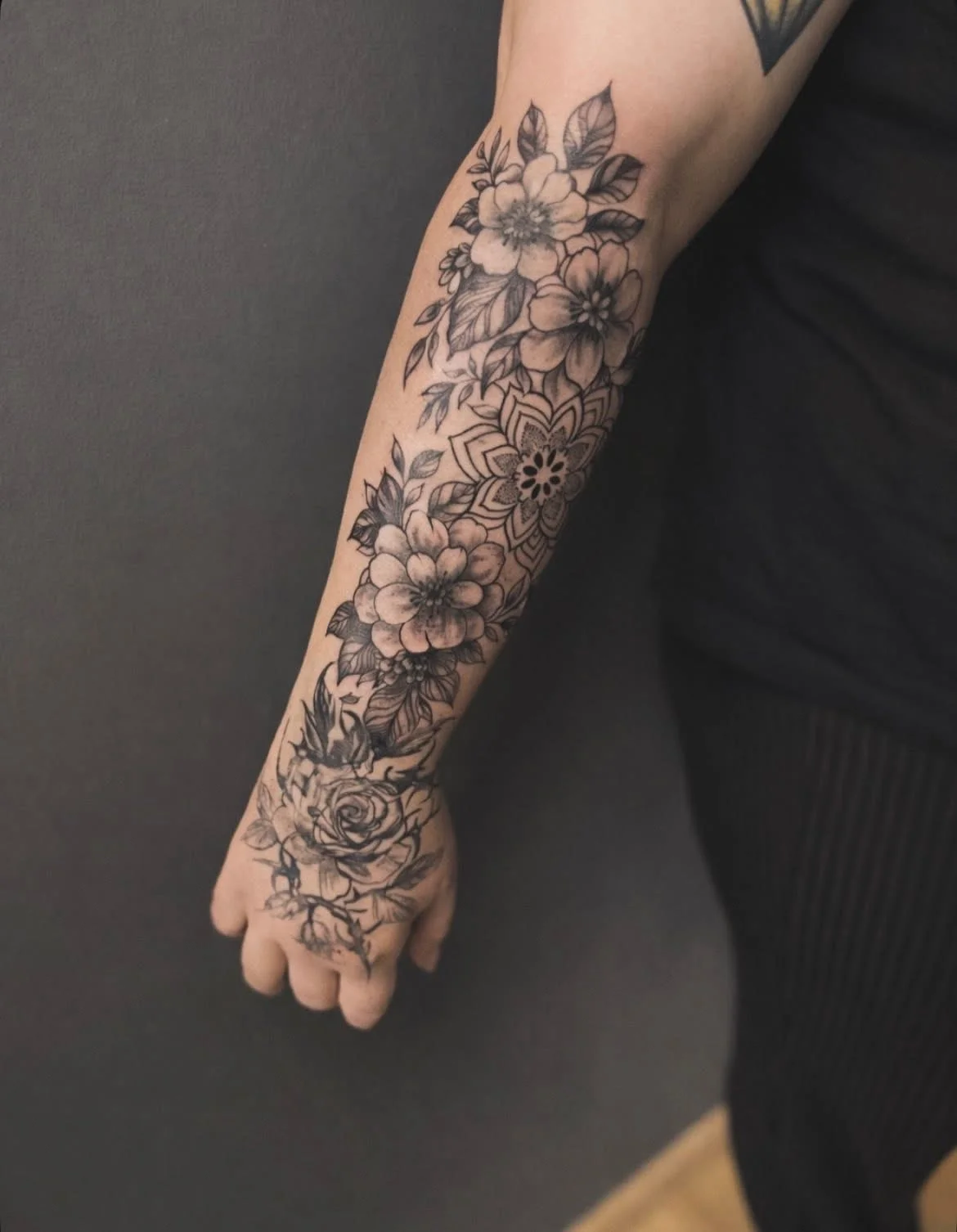 Black and grey floral sleeve tattoo with mandala on forearm and hand