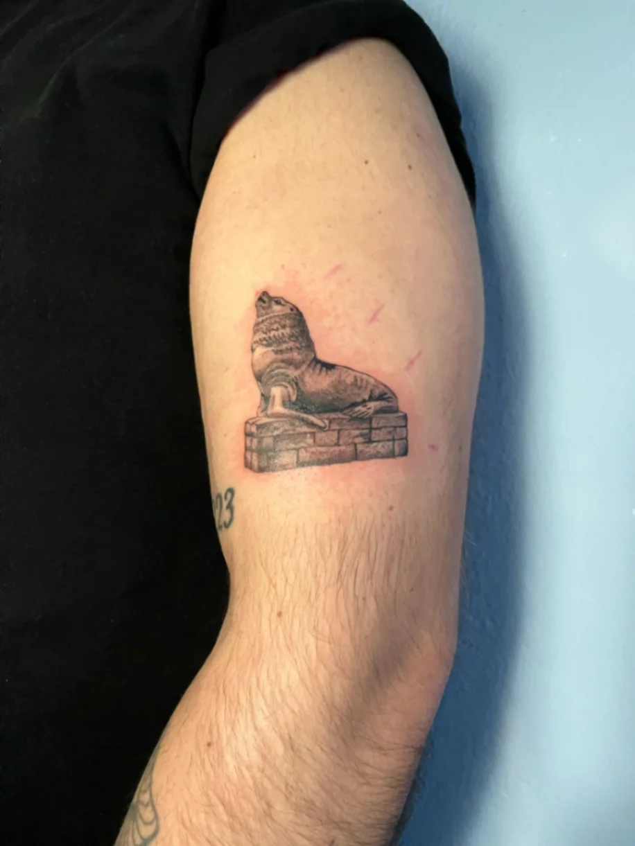 Black and grey sea lion statue tattoo on upper arm