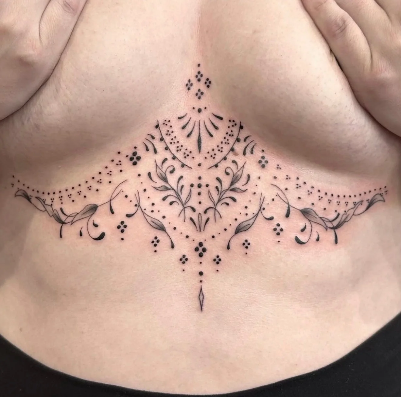 Ornamental floral and dotwork sternum tattoo with symmetrical botanical motifs