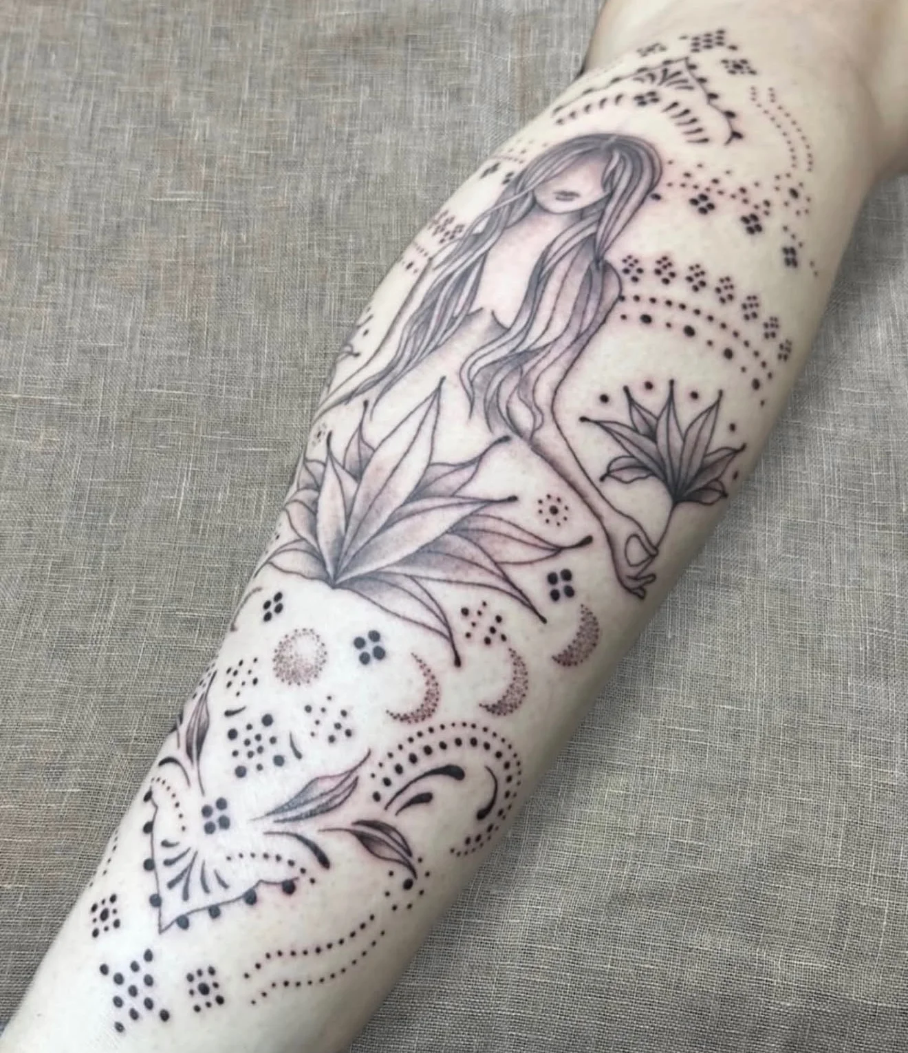 Fine line fairy figure with floral and dotwork elements on forearm