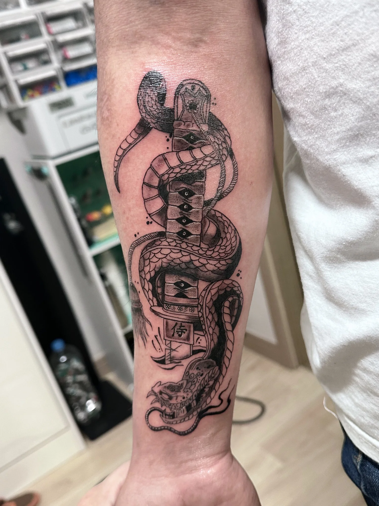 Black and grey snake coiled around katana and lantern on forearm
