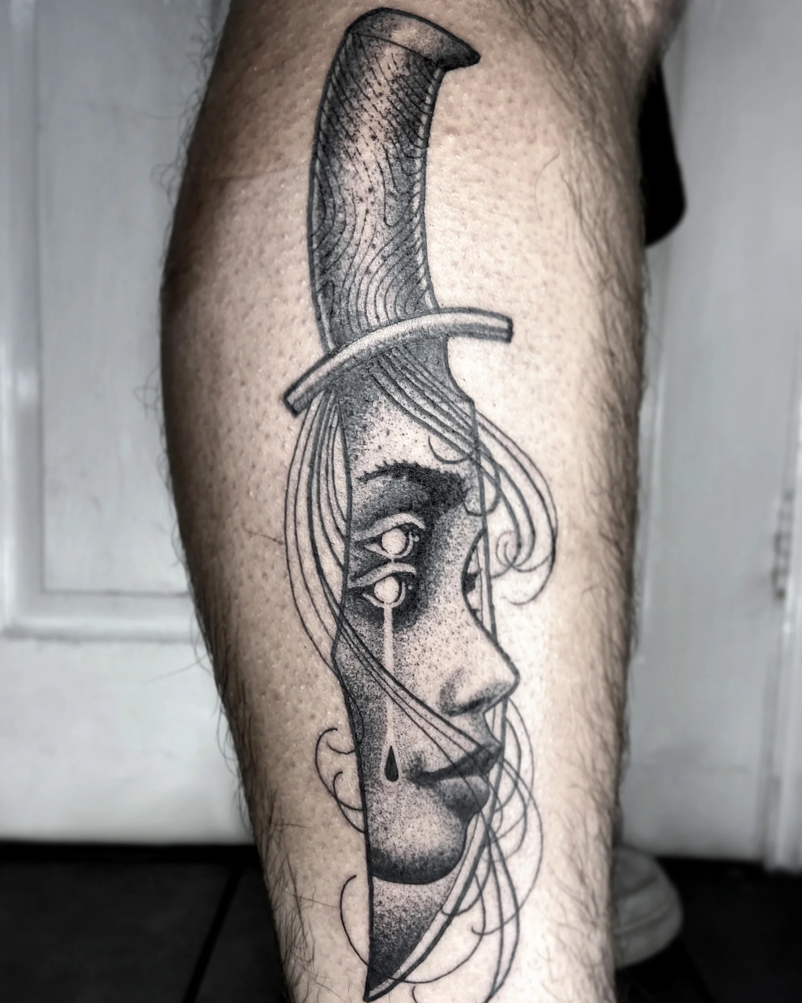 Black and grey illustrative dagger with crying face on calf