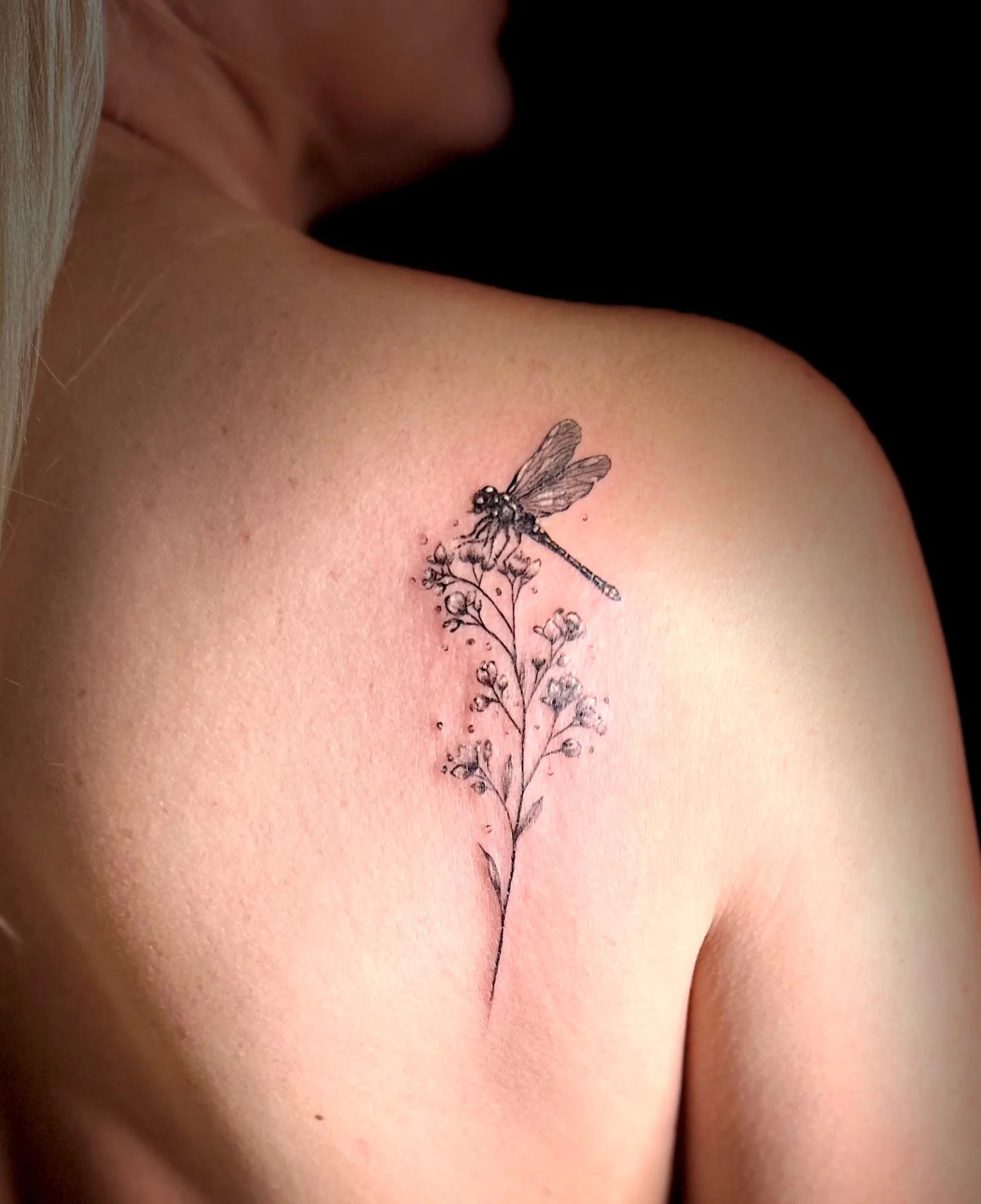 Fine line dragonfly and wildflower sprig tattoo on upper back