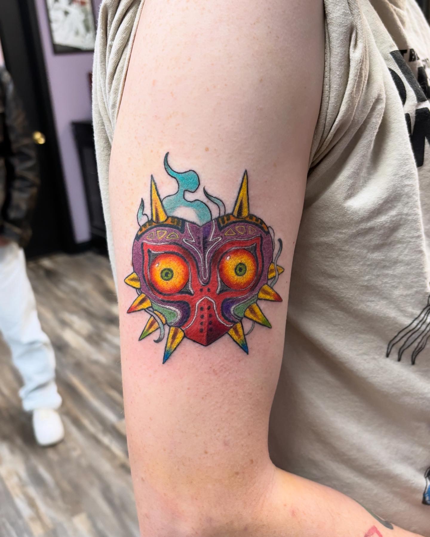 Colorful Majora's Mask video game tattoo with glowing eyes on upper arm