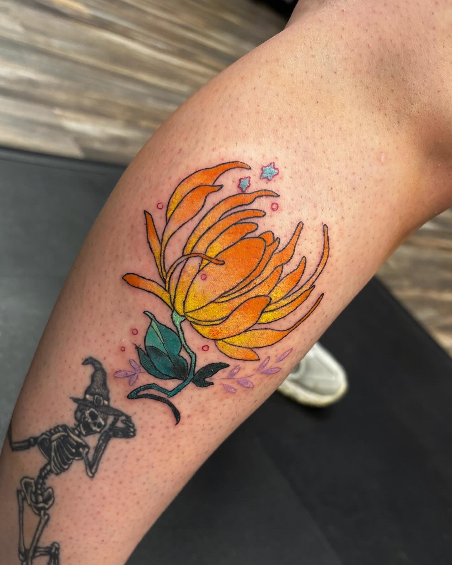 Vibrant orange protea flower tattoo with decorative elements on forearm