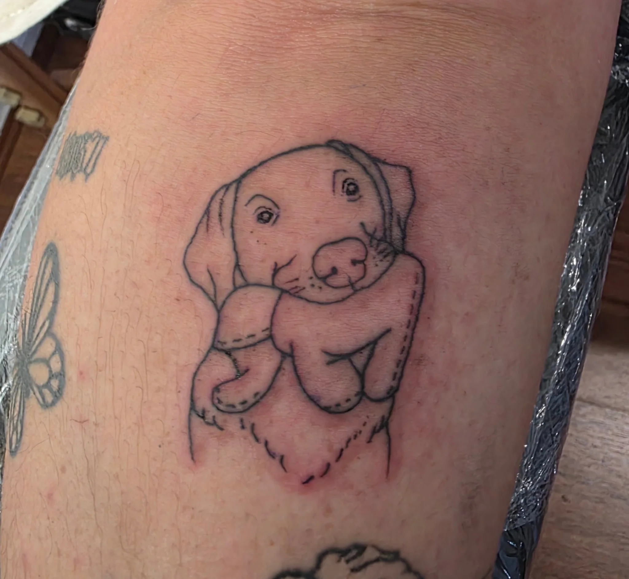 Fine line puppy hugging stuffed animal tattoo on wrist