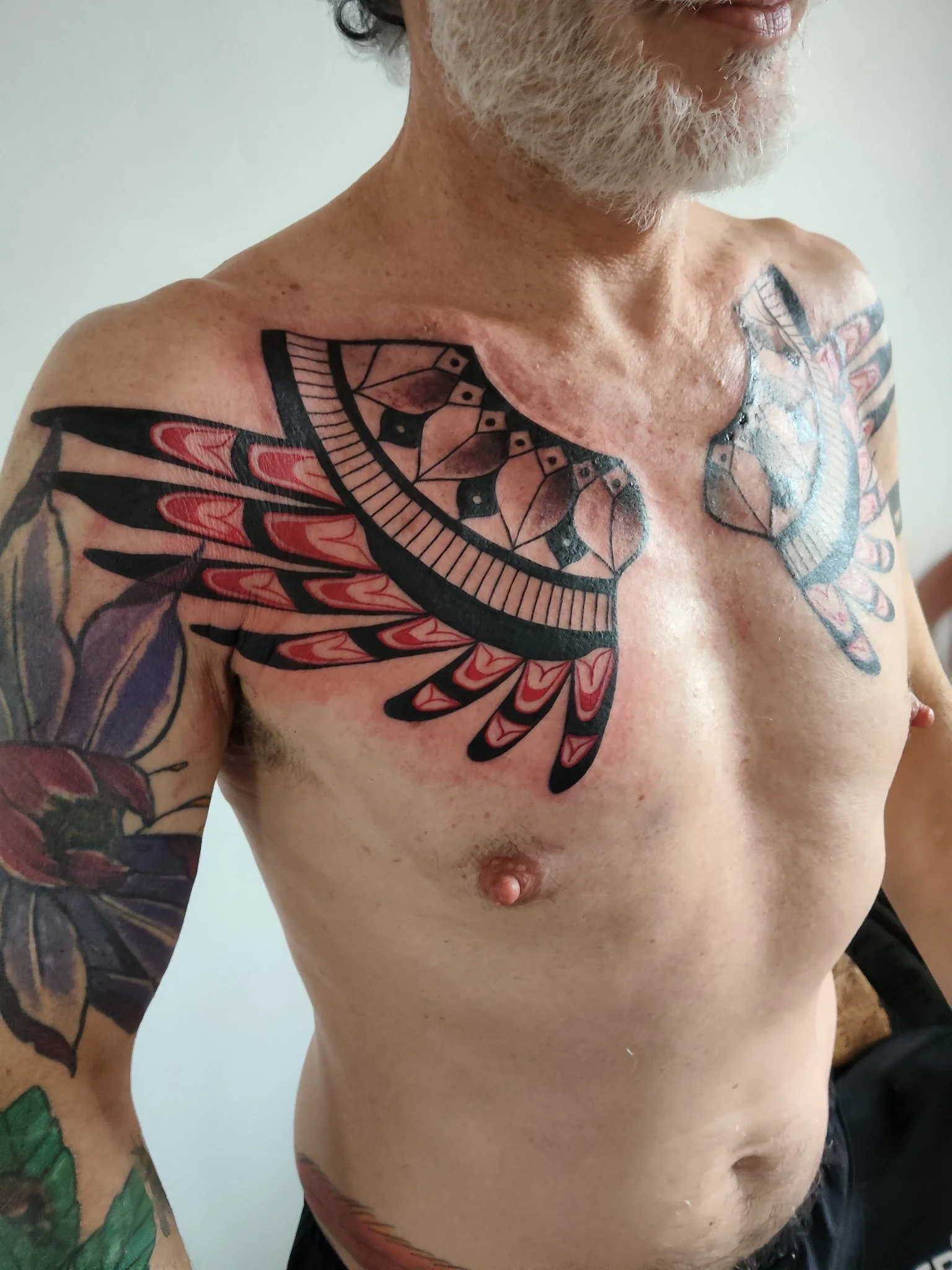 Neo-traditional geometric wing tattoo across chest and shoulder