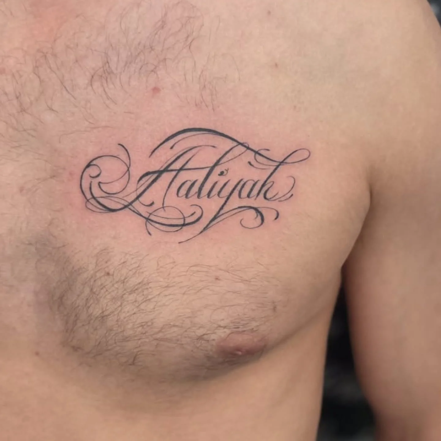 Ornate calligraphy name tattoo with flourishes on chest