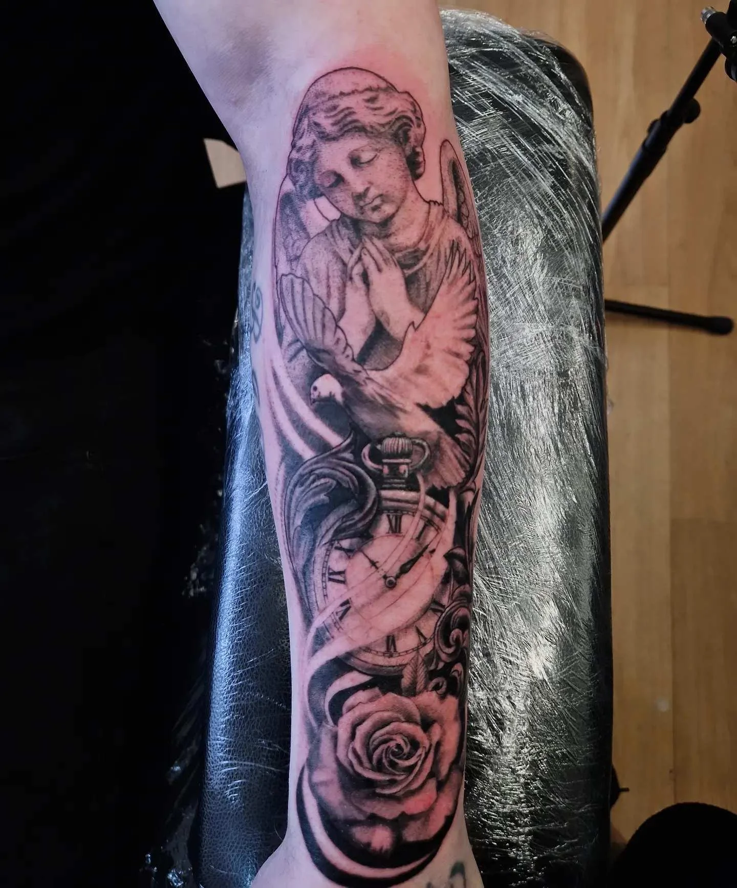 Black and grey realism angel with dove, clock, and rose on forearm