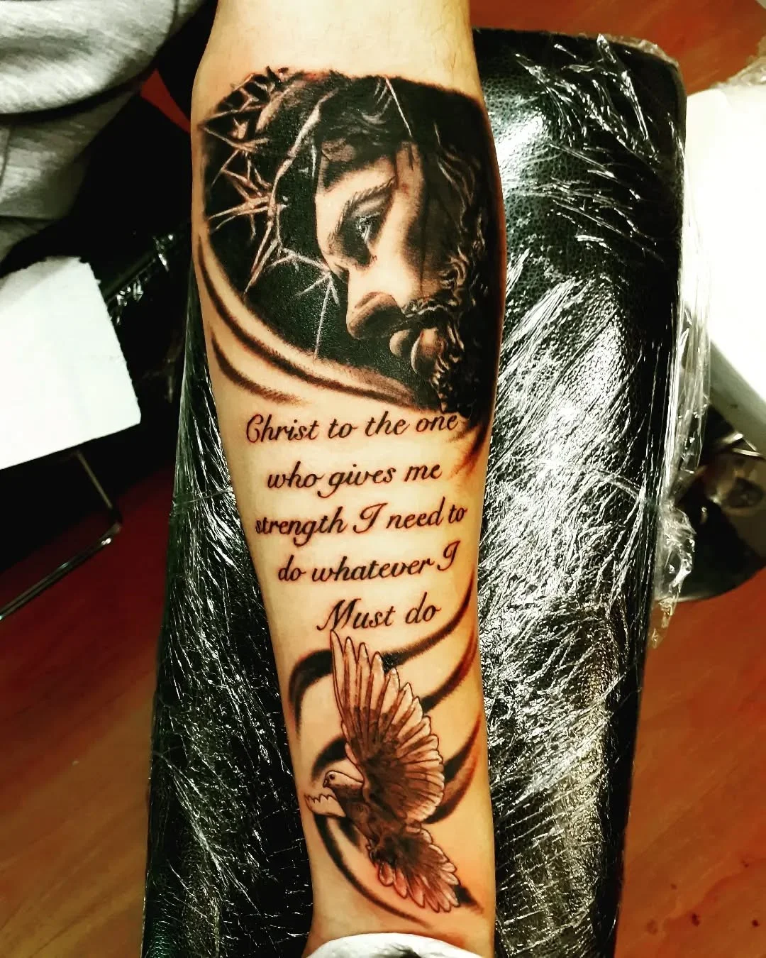 Black and grey realism Jesus portrait with script and dove on forearm