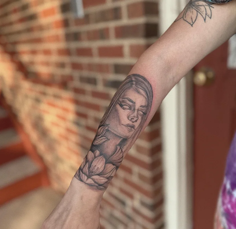 Black and grey realism portrait of woman with lotus flowers on forearm