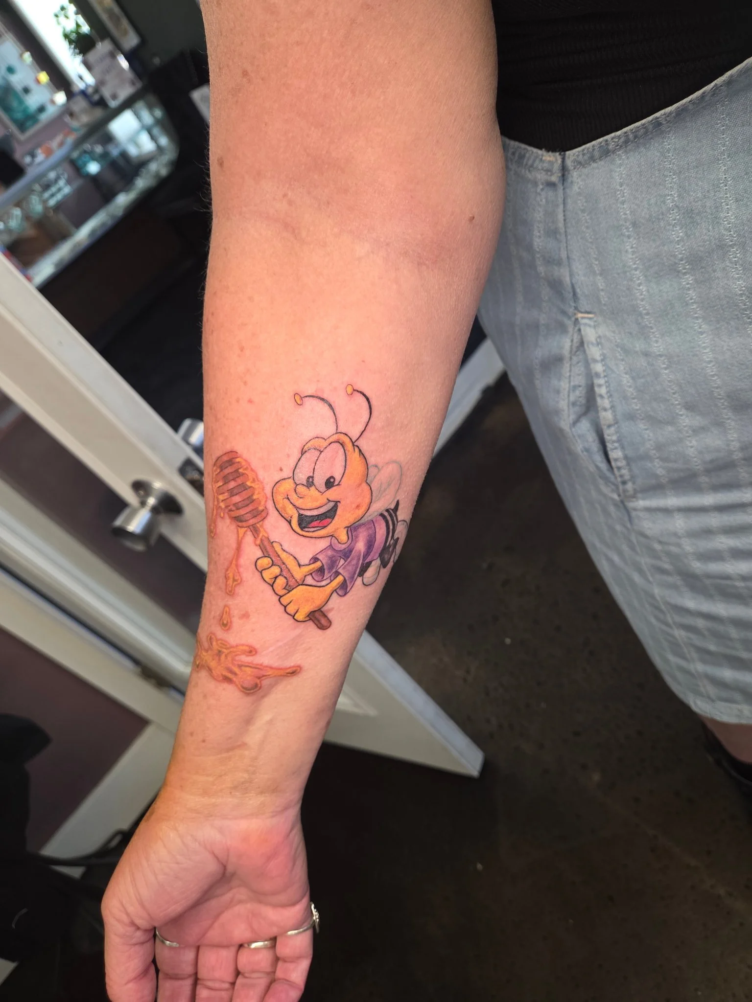 New school cartoon bee with honey dipper tattoo on forearm