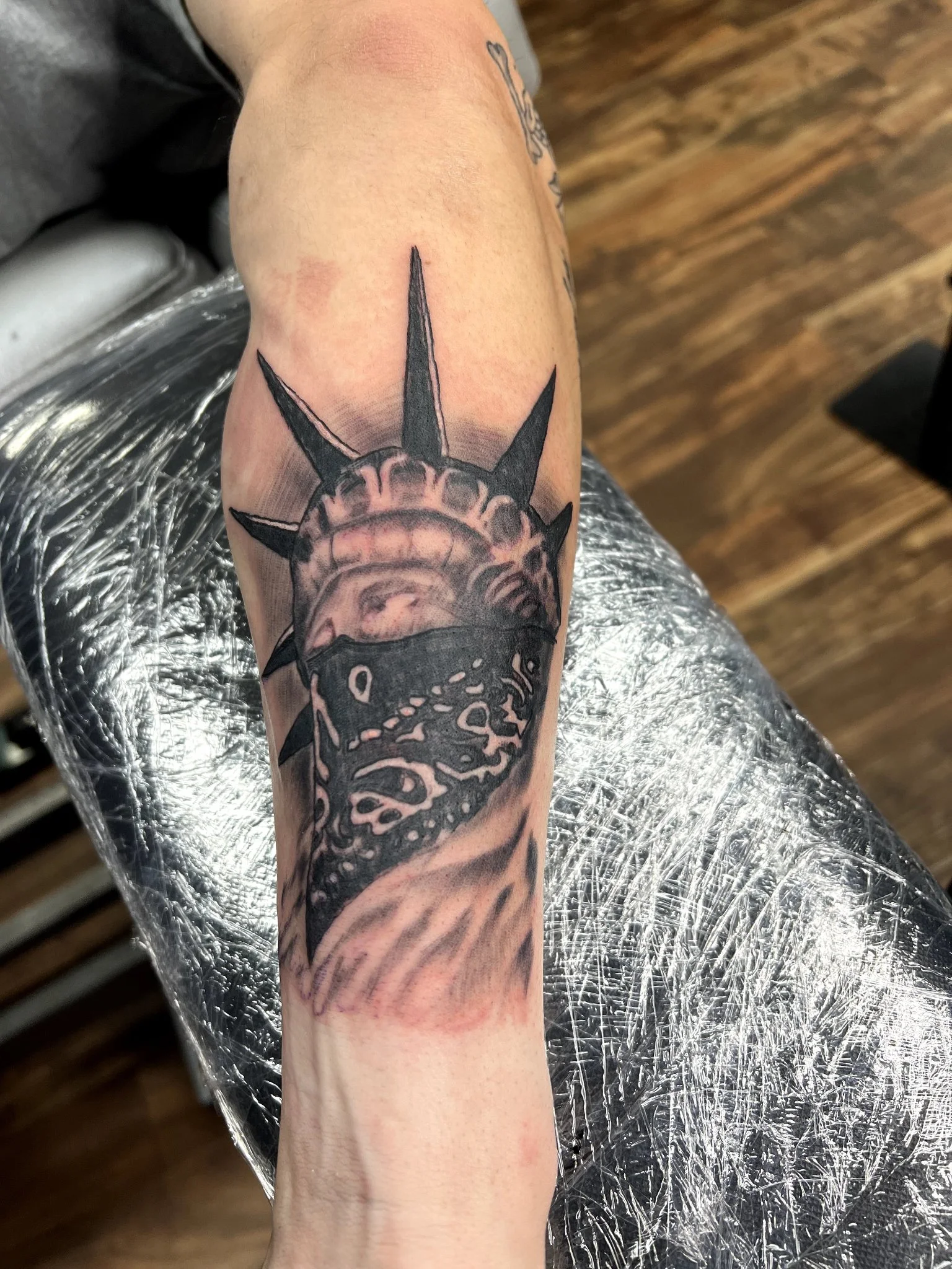 Black and grey Statue of Liberty with bandana mask tattoo on forearm