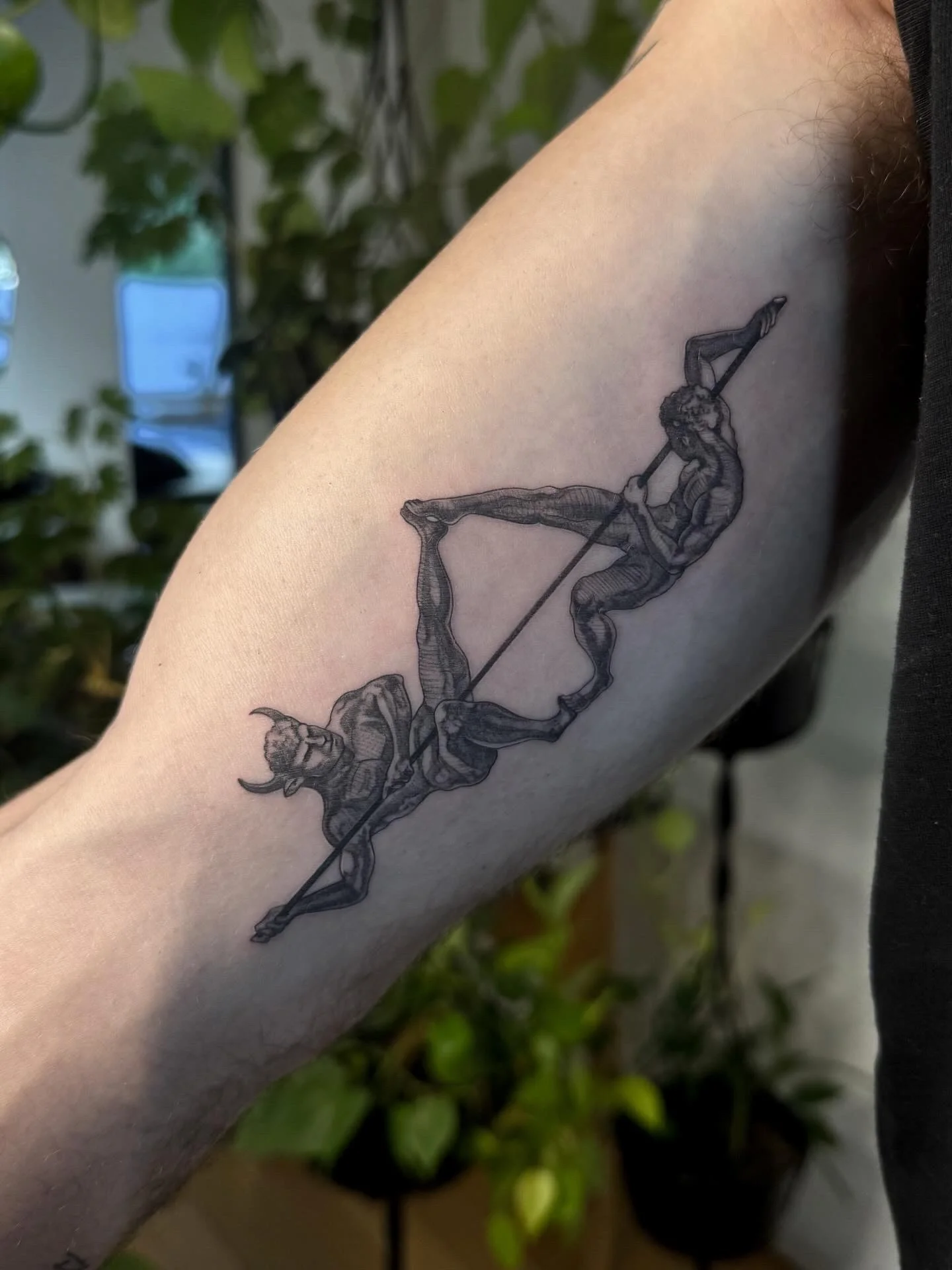 Illustrative black ink mythology figures forming bow and arrow on upper arm