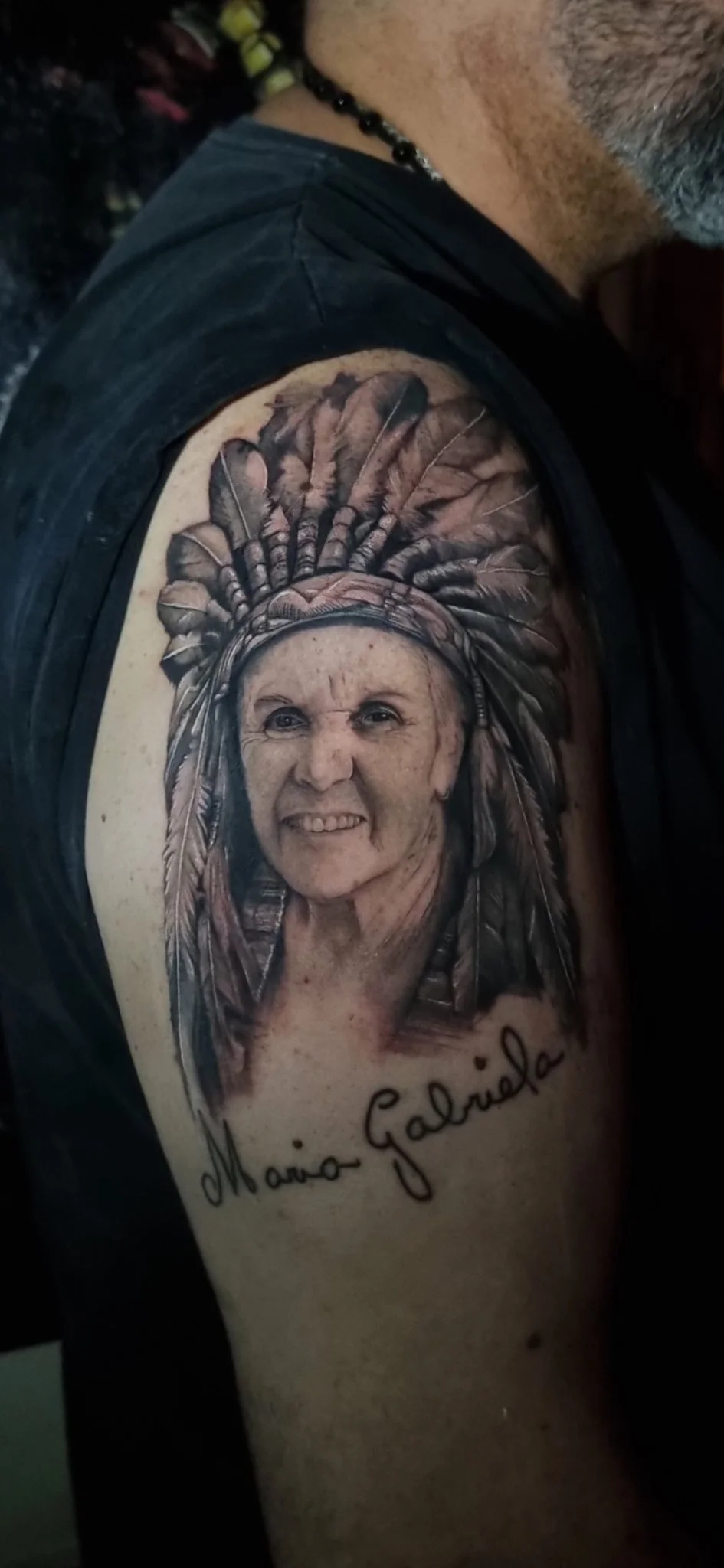 Black and grey realism portrait tattoo of elderly woman with feathered headdress on upper arm