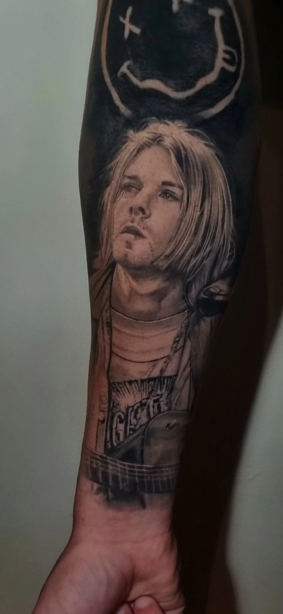 Black and grey realism portrait tattoo on forearm with band logo