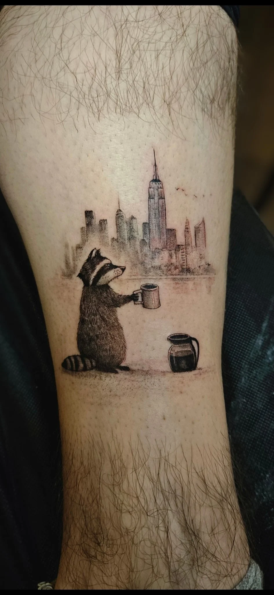 Fine line raccoon with coffee mug and New York skyline on forearm