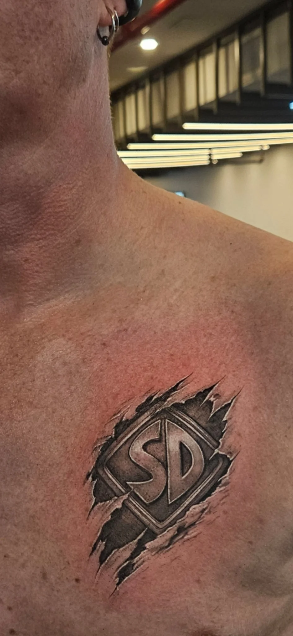 Black and grey ripped skin SD logo tattoo on chest