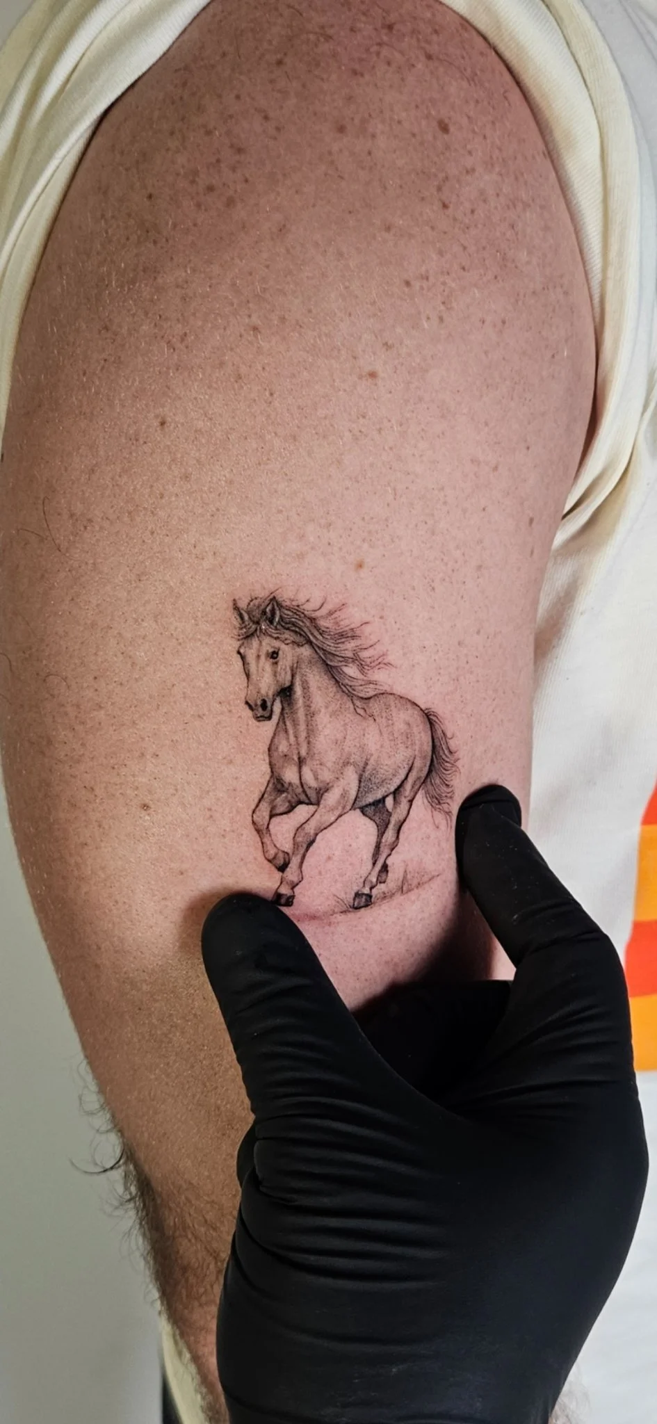 Fine line black and grey running horse tattoo on upper arm