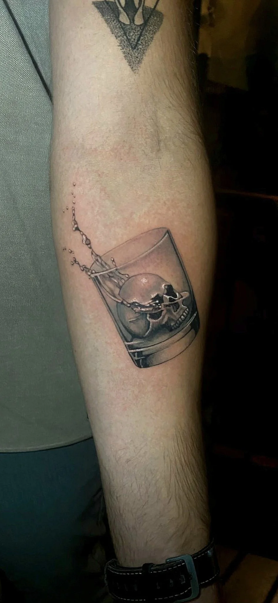 Black and grey realism whiskey glass with skull ice cube on forearm