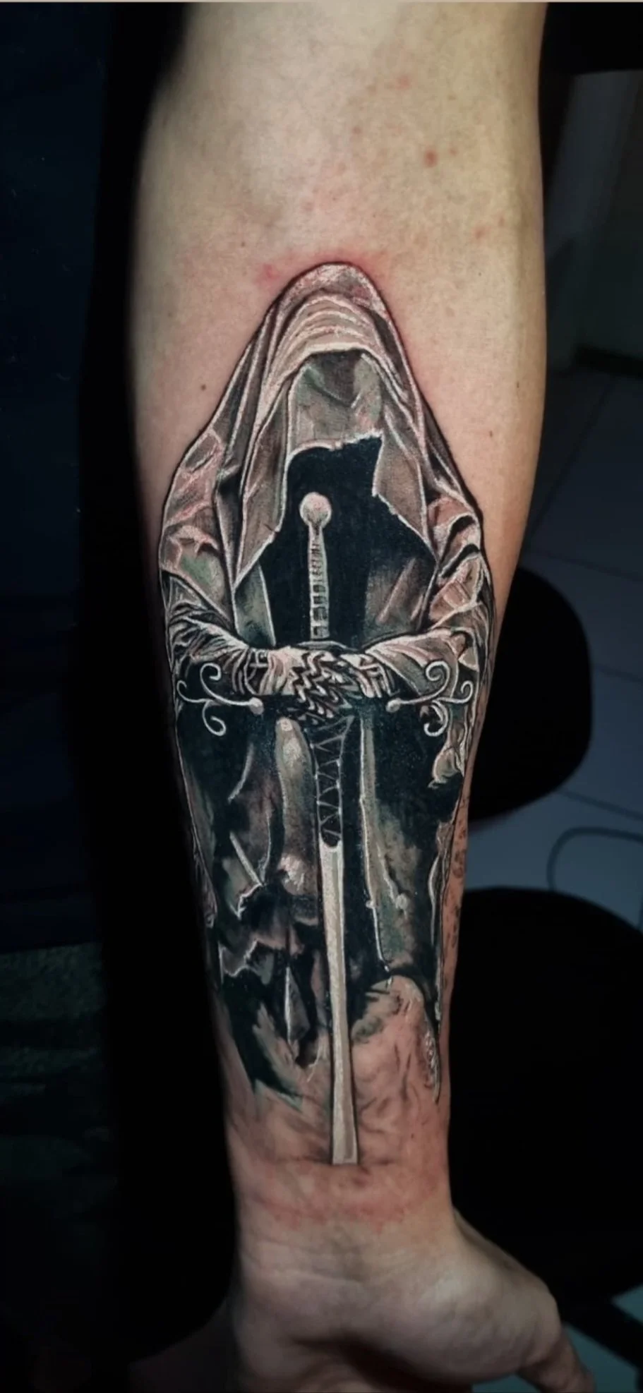 Black and grey realism hooded wraith with sword tattoo on forearm