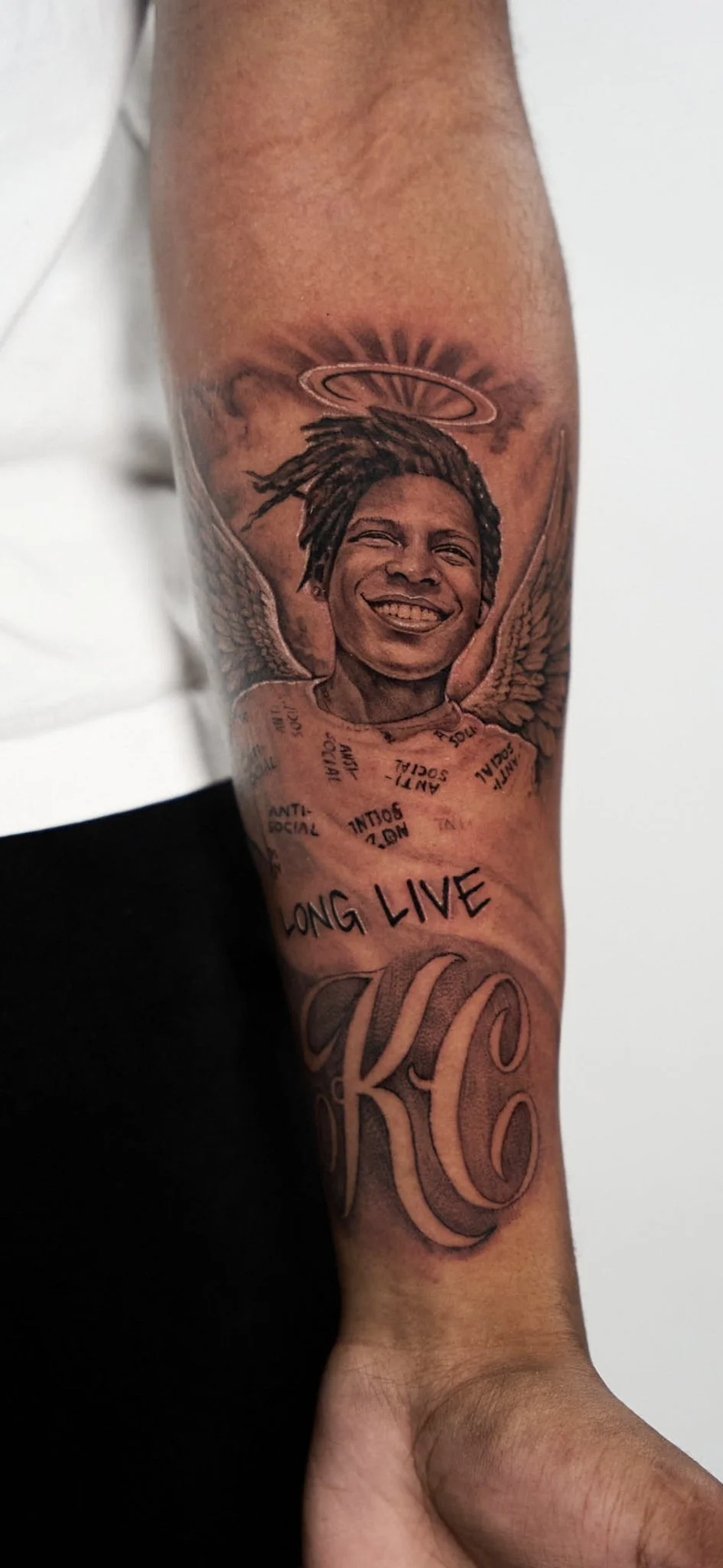 Black and grey realism memorial portrait tattoo with angel wings on forearm