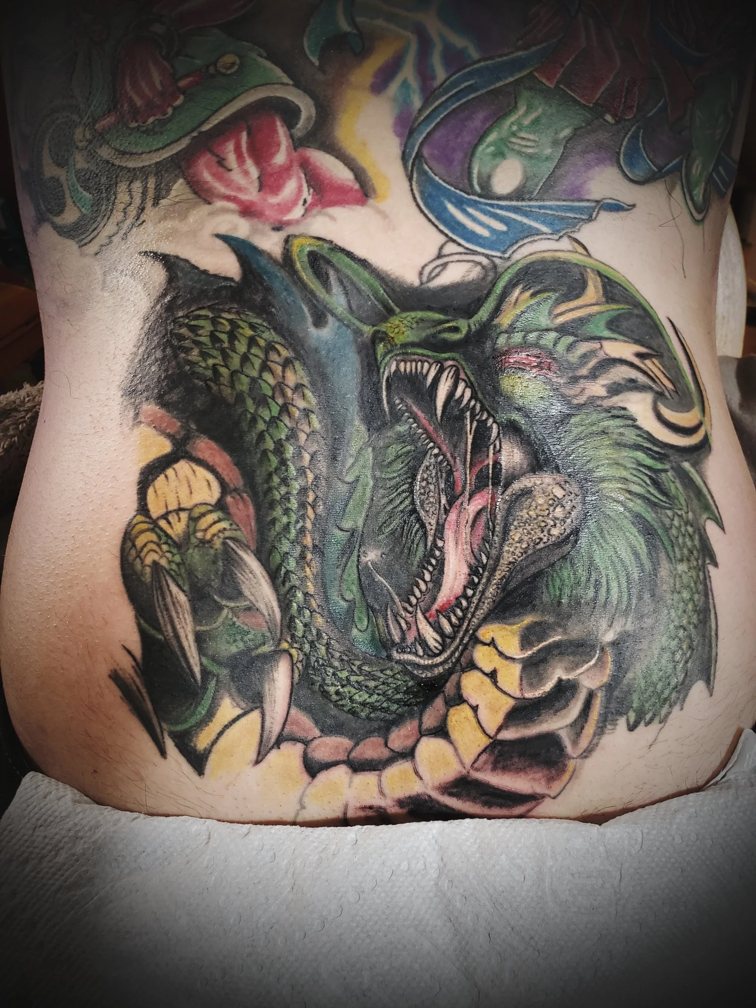 Large colorful dragon creature tattoo on abdomen and lower back