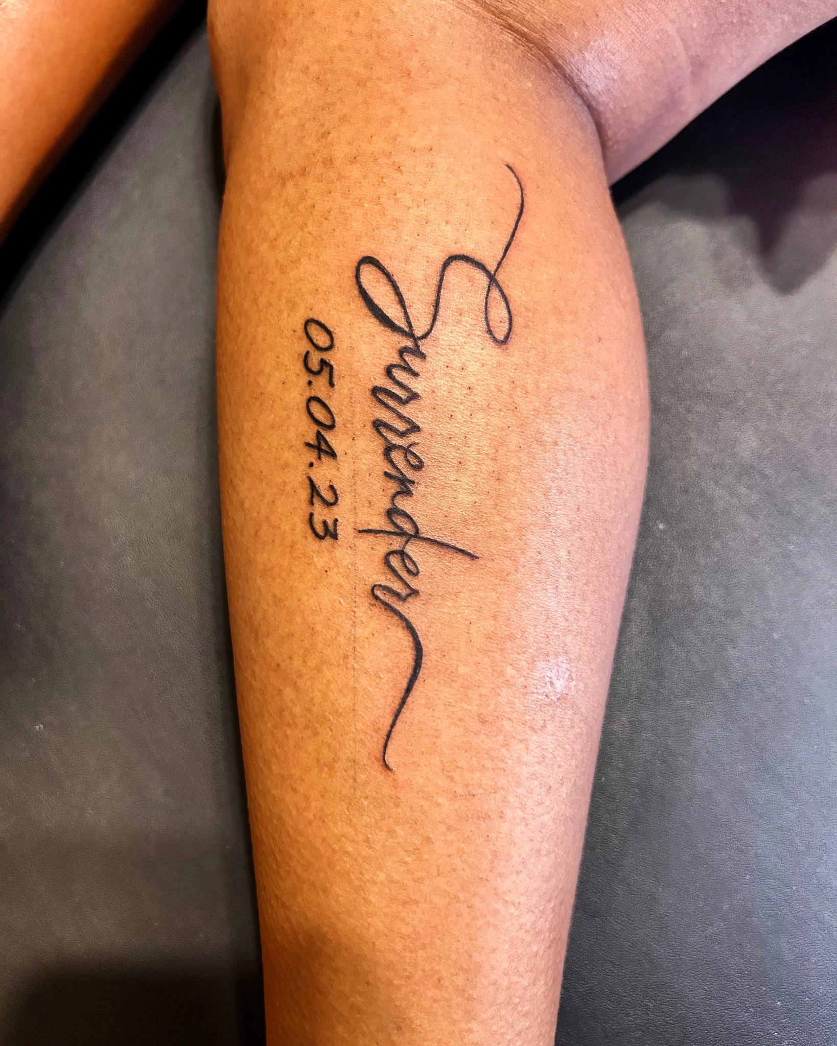 Calligraphy script surrender tattoo with date on forearm