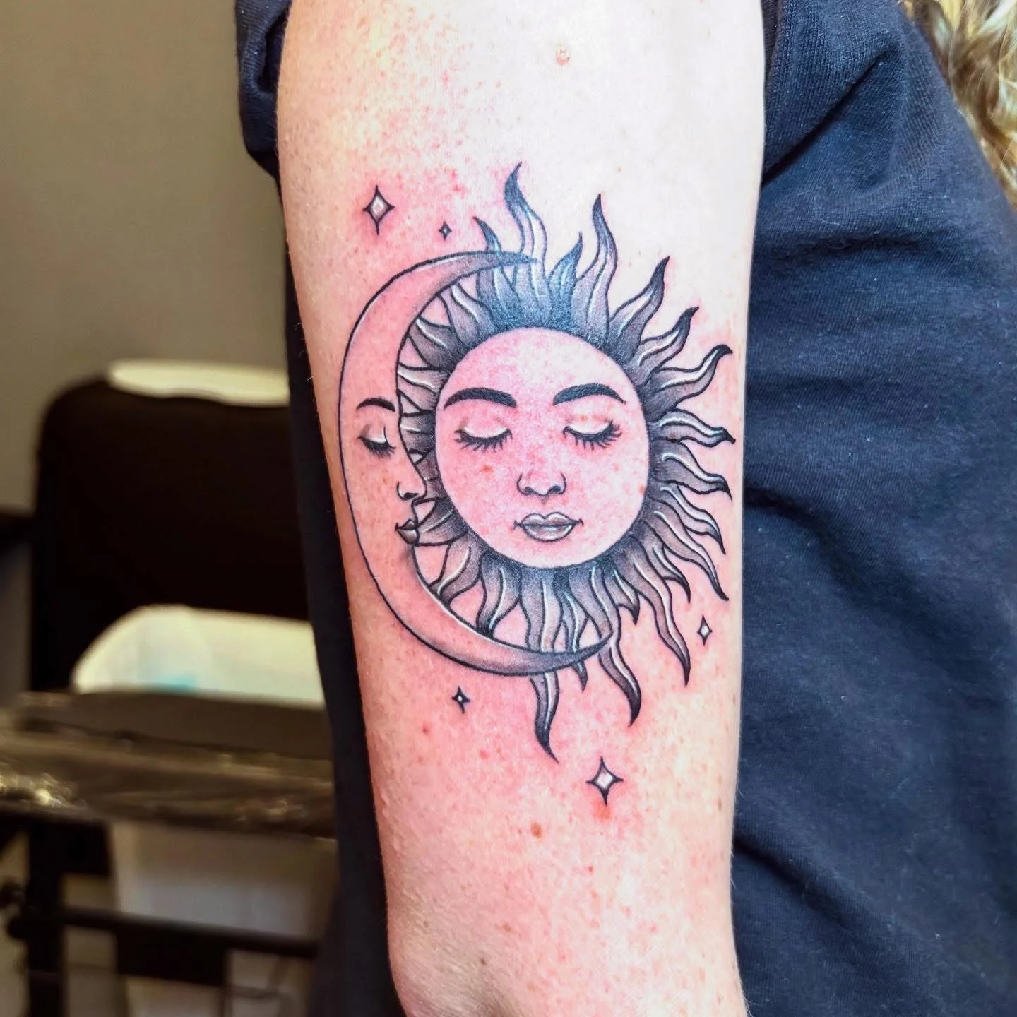 Neo-traditional sun and moon face tattoo on upper arm