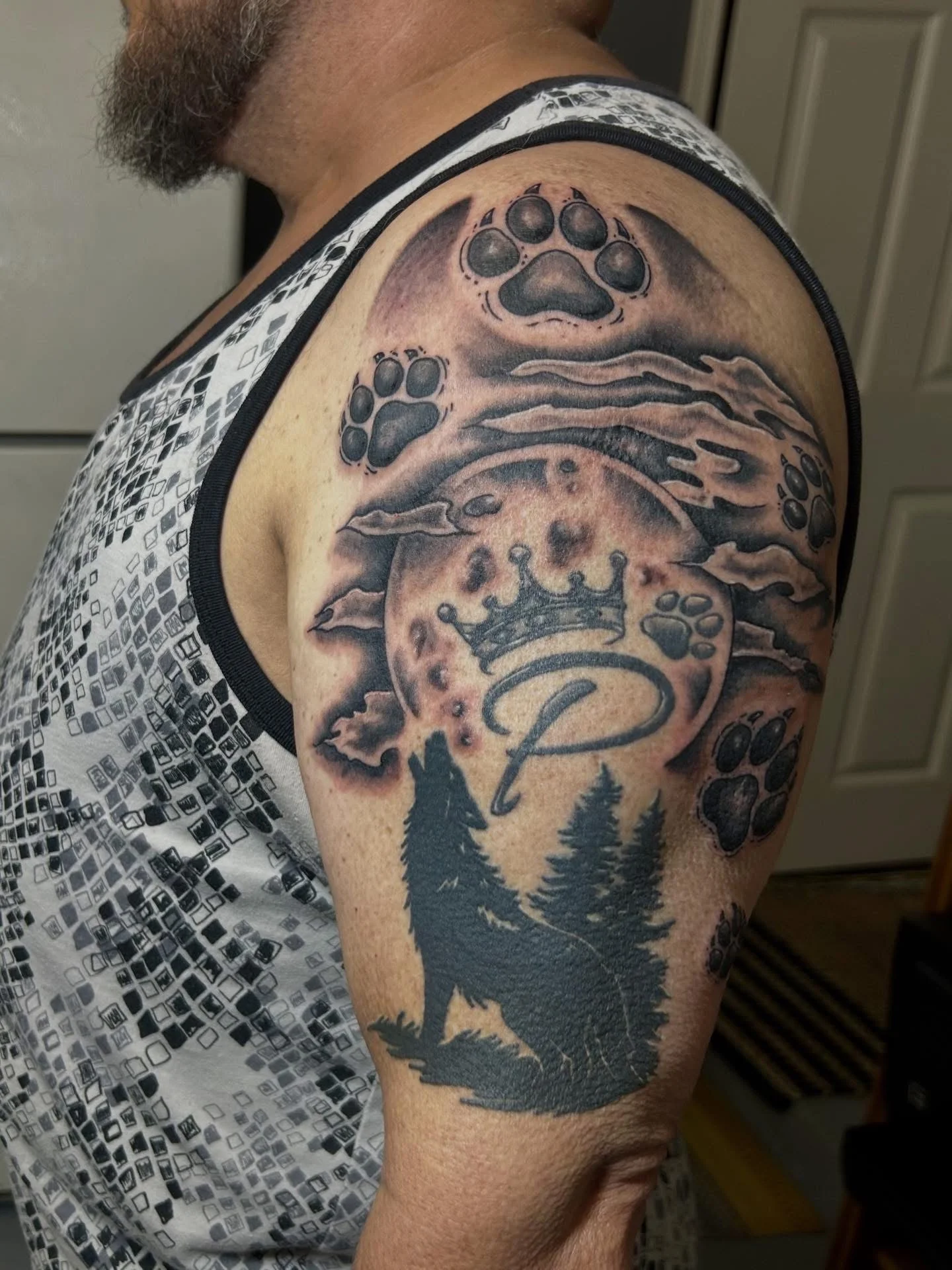 Black and grey wolf howling at crowned moon with paw prints on upper arm