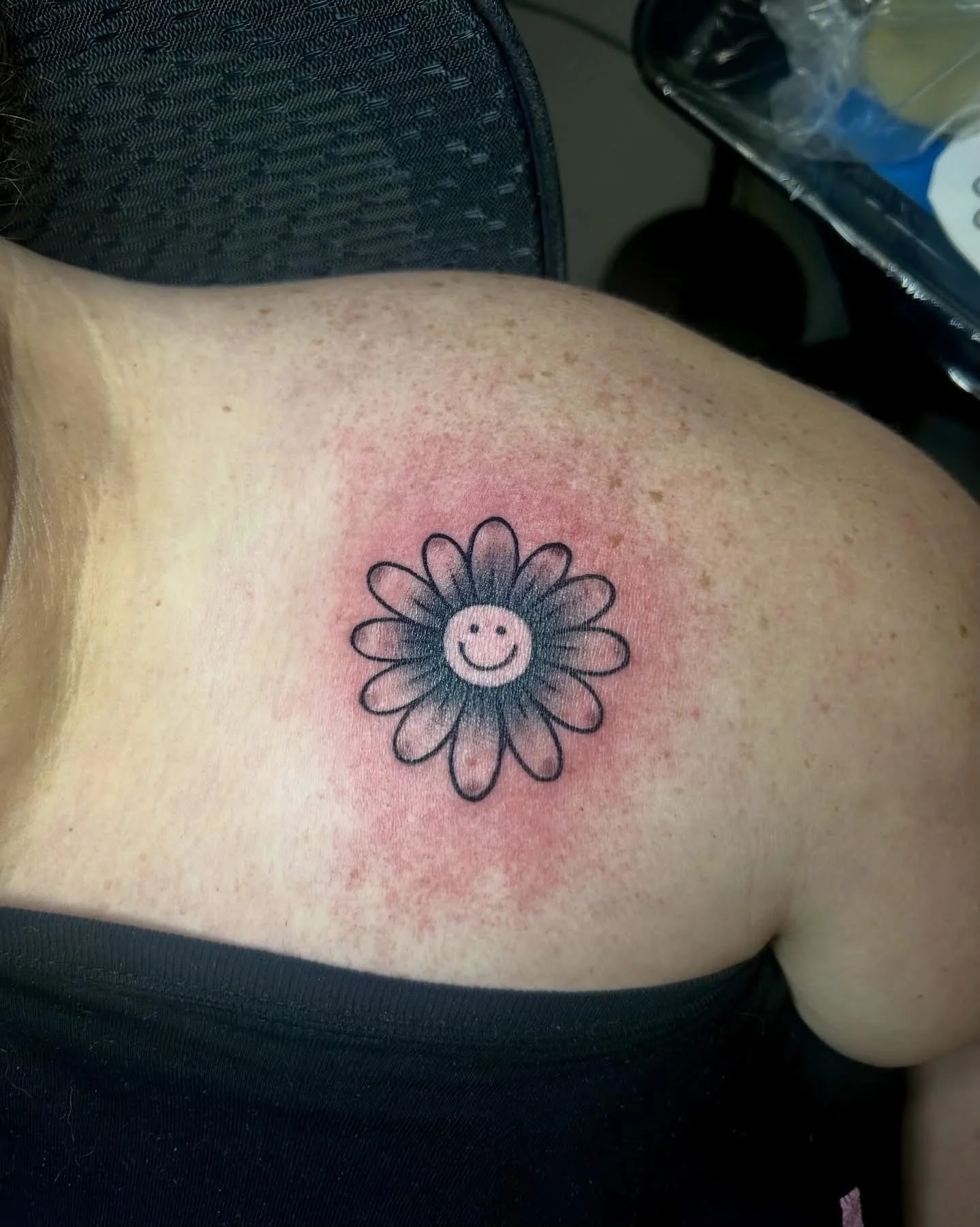 Black and grey daisy with smiley face center on upper back