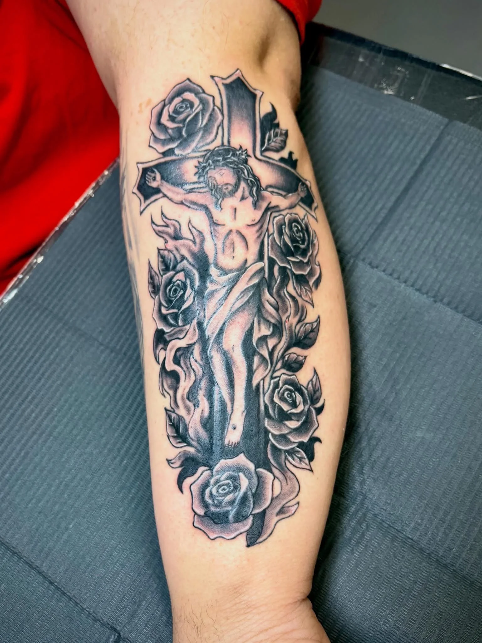 Black and grey crucifixion with roses tattoo on lower leg