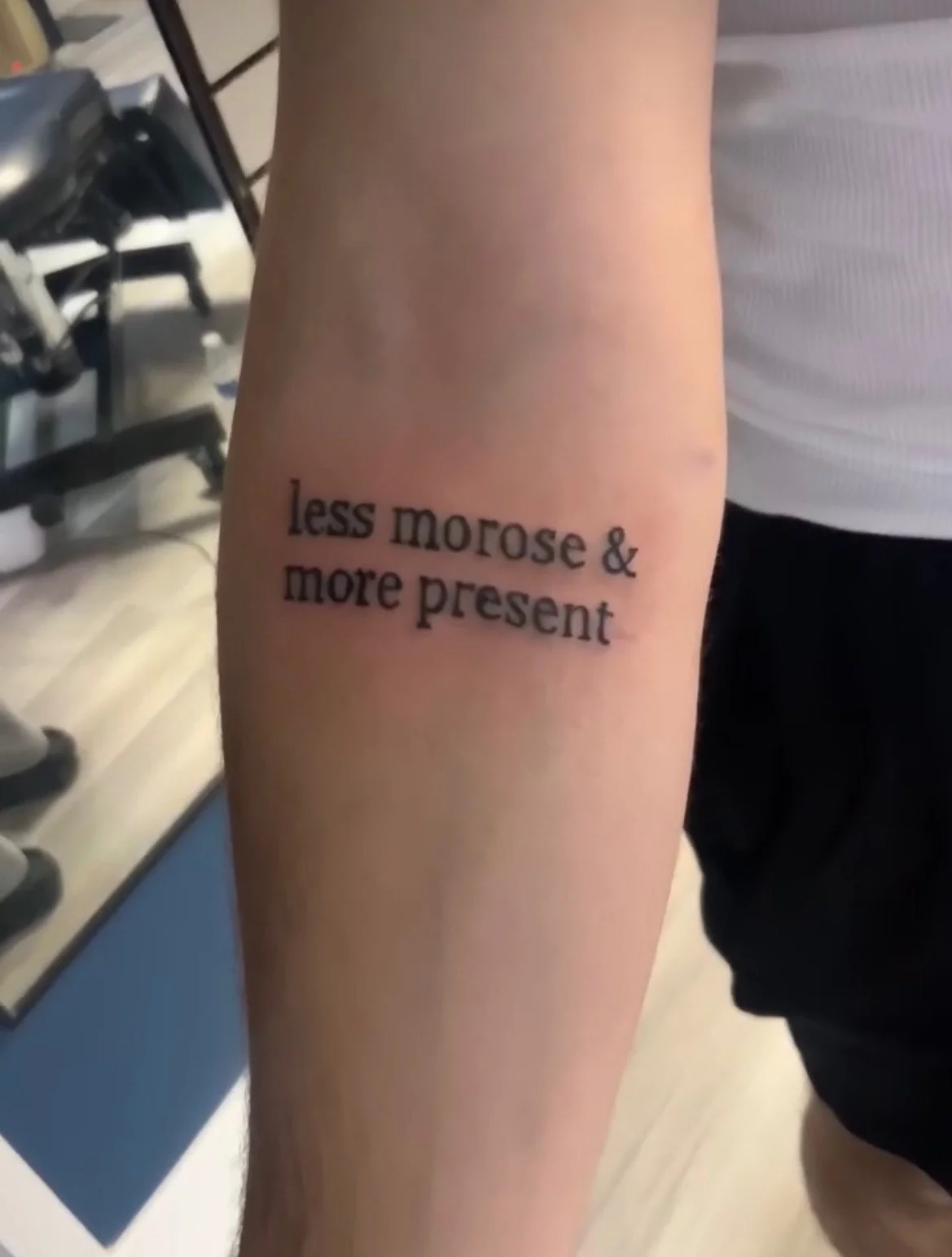 Black serif lettering quote tattoo on inner forearm