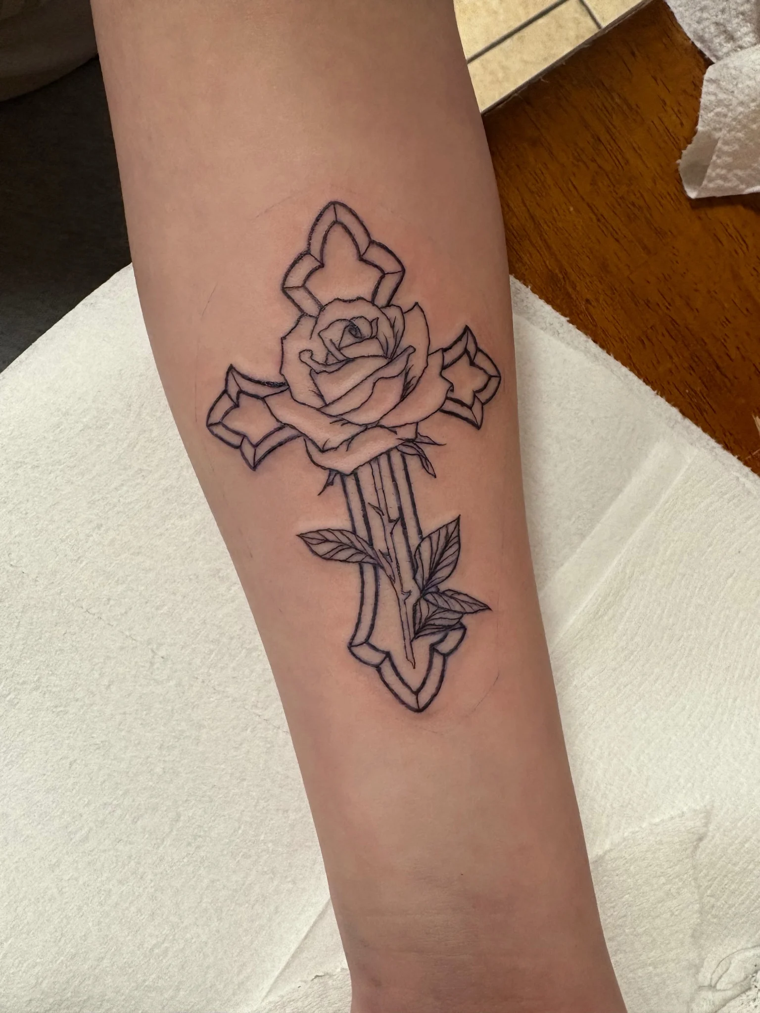 Neo-traditional cross and rose outline tattoo on forearm
