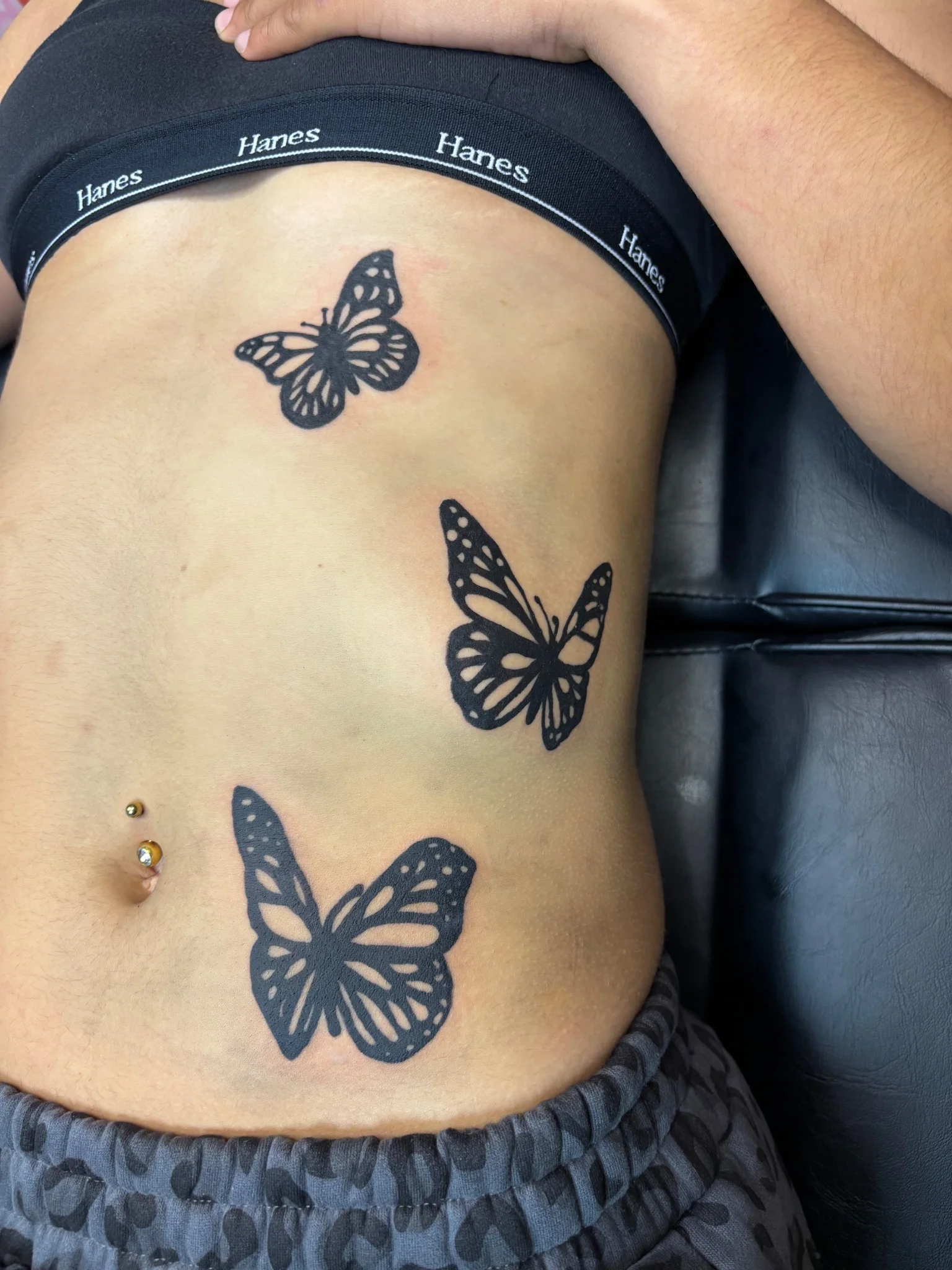 Three black monarch butterfly tattoos on the stomach and side
